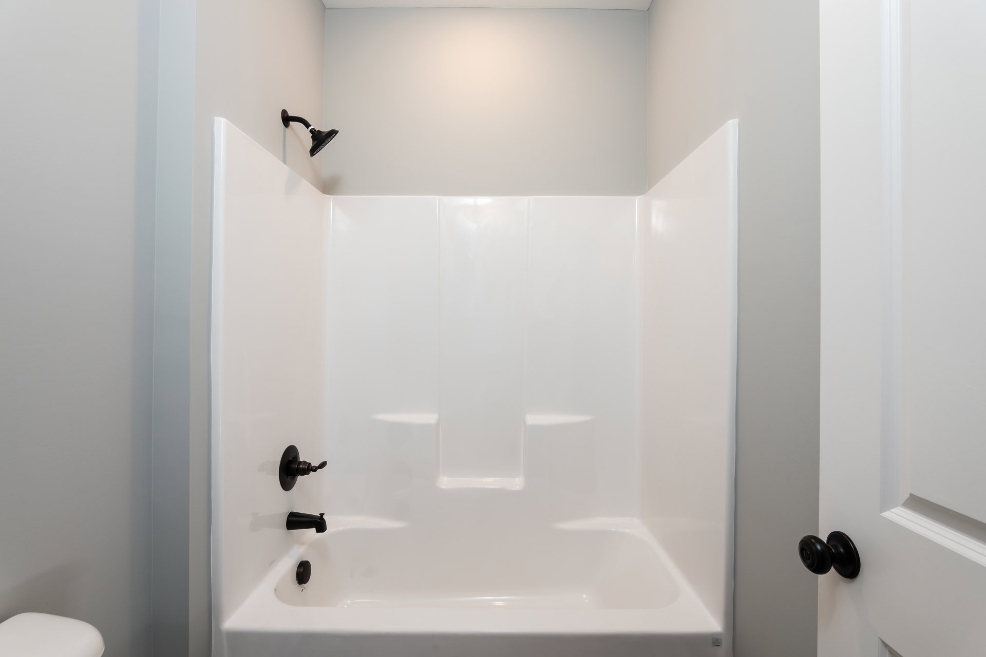 Freestanding white bathtub with chrome faucet beside tiled wall, black door knob on white wall, glossy surfaces reflecting light