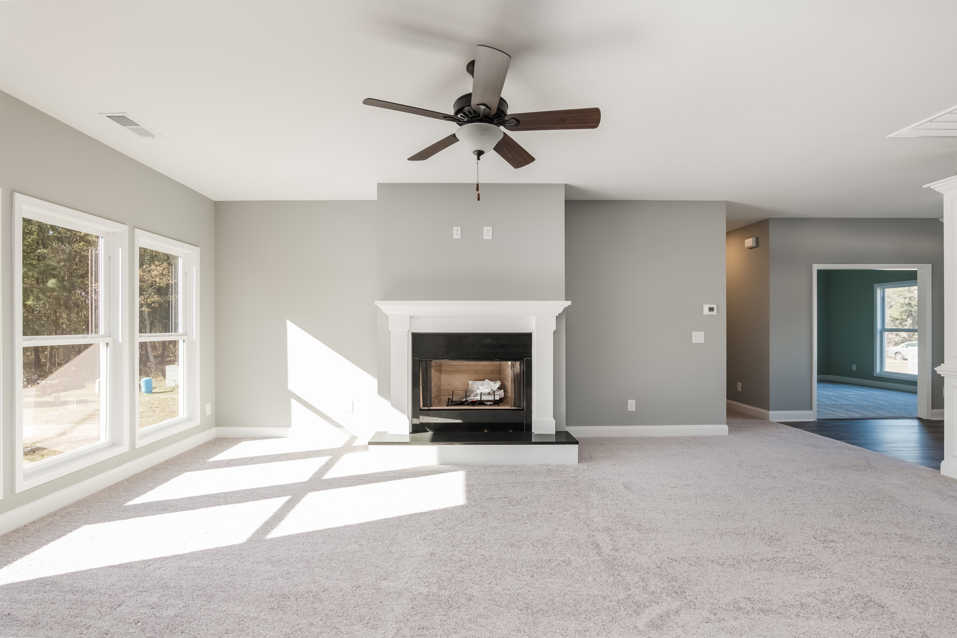 Living room with carpet flooring, white fireplace featuring a black glass door, and ceiling fan with light fixture