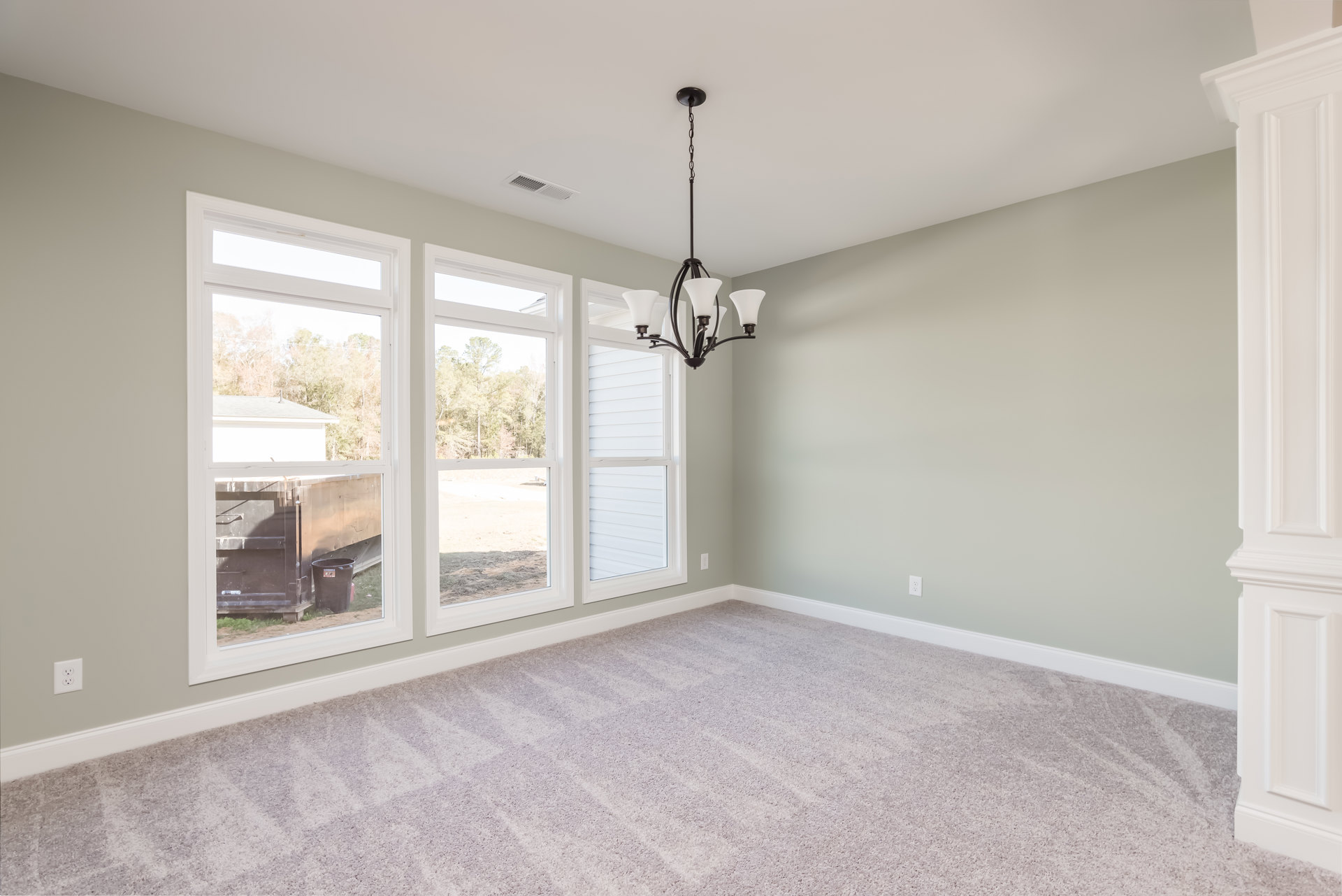 Chandelier hanging from ceiling in carpeted room with large windows, white door, white molding, and neutral walls