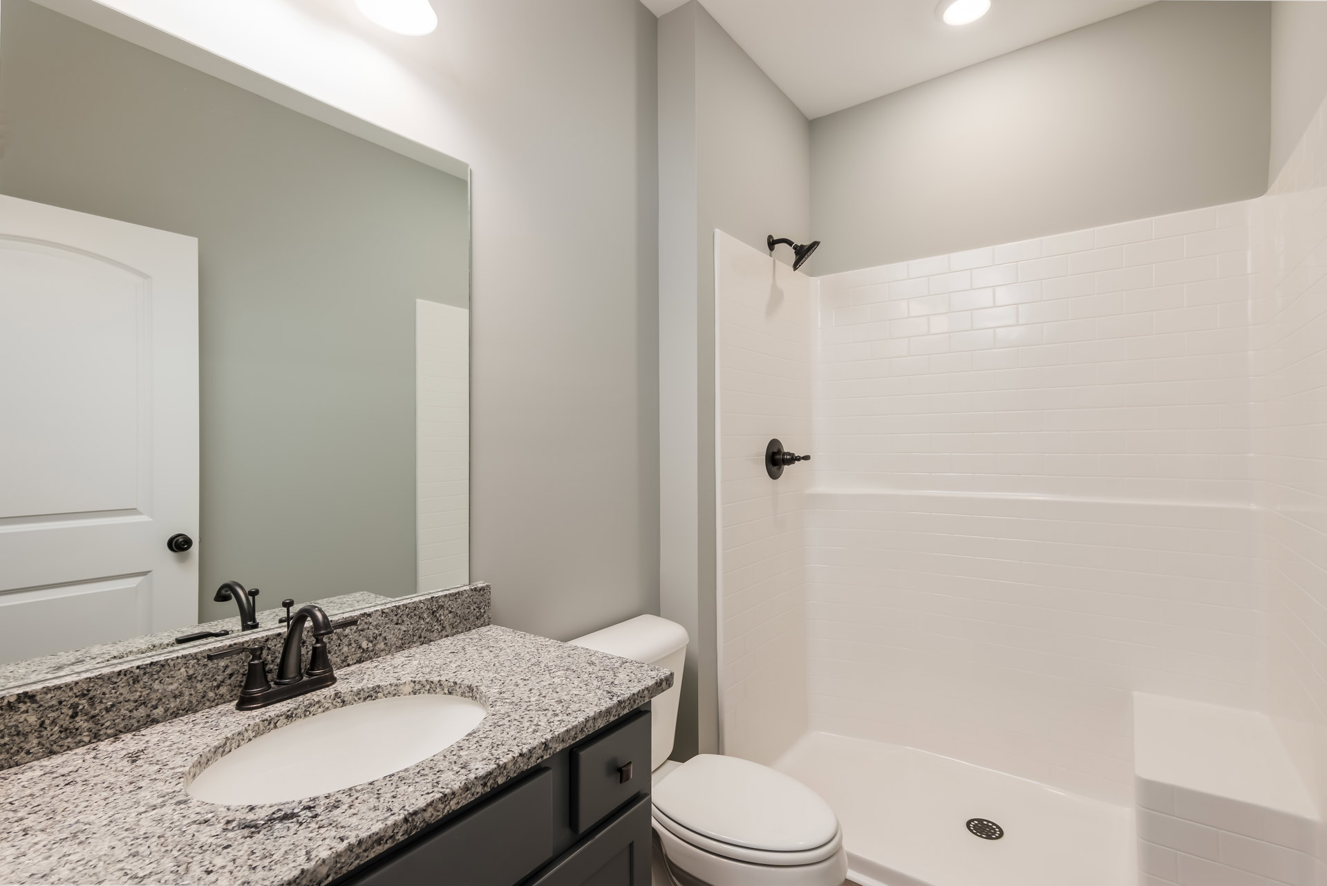 Modern bathroom featuring a white sink with black faucet and tray, tiled walls, glass-enclosed shower, and white toilet adjacent to a minimalist vanity cabinet.