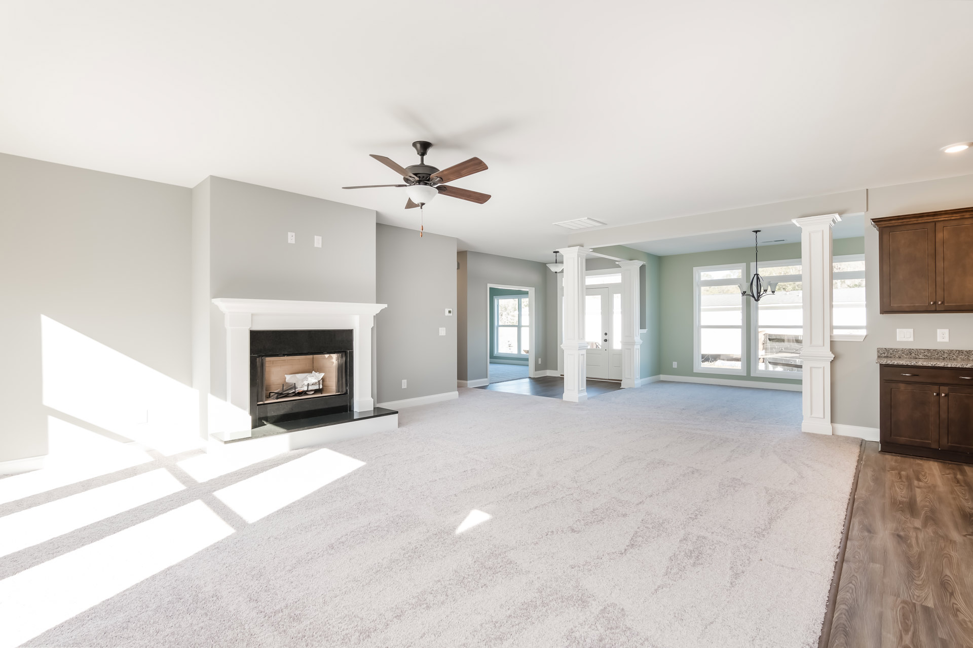 Living room with wood flooring, white-framed fireplace containing decorative logs, ceiling fan with light fixture, built-in cabinetry along the wall
