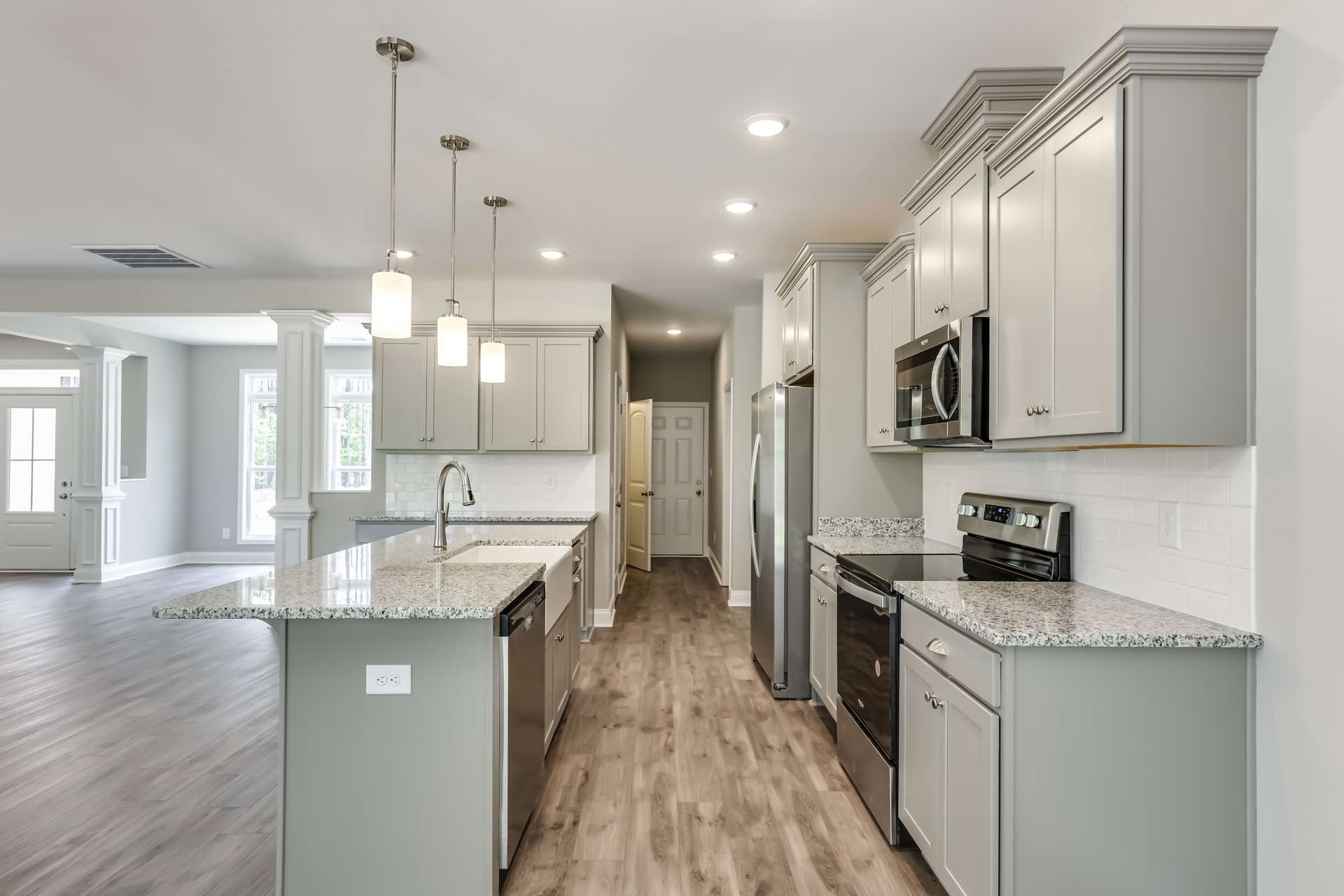 Kitchen with granite countertops, wood flooring, stainless steel appliances including microwave, refrigerator, stove, kitchen island with sink, white door with black handle, and