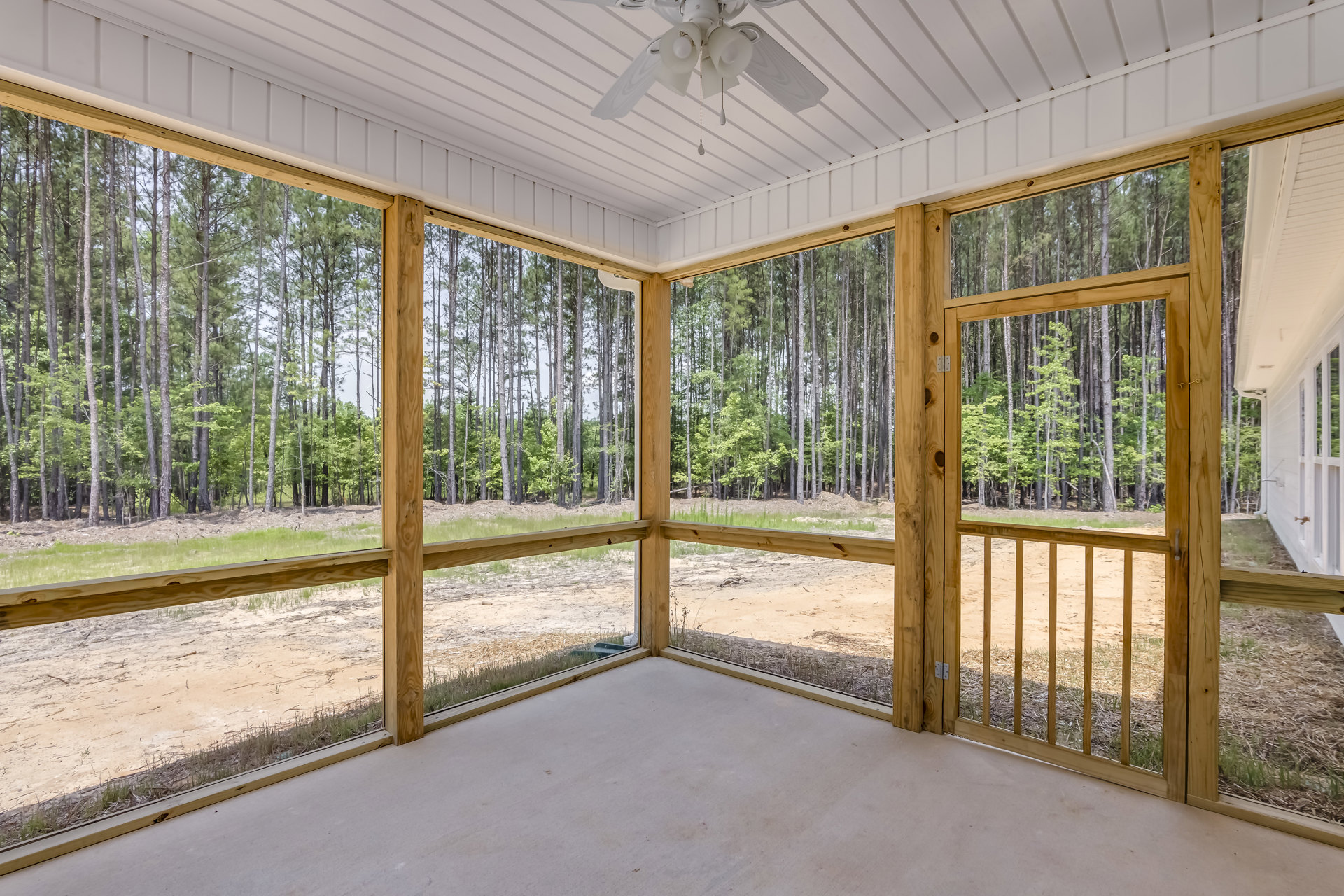 Covered porch with white ceiling fan, screen door, and view of trees and dirt yard in background
