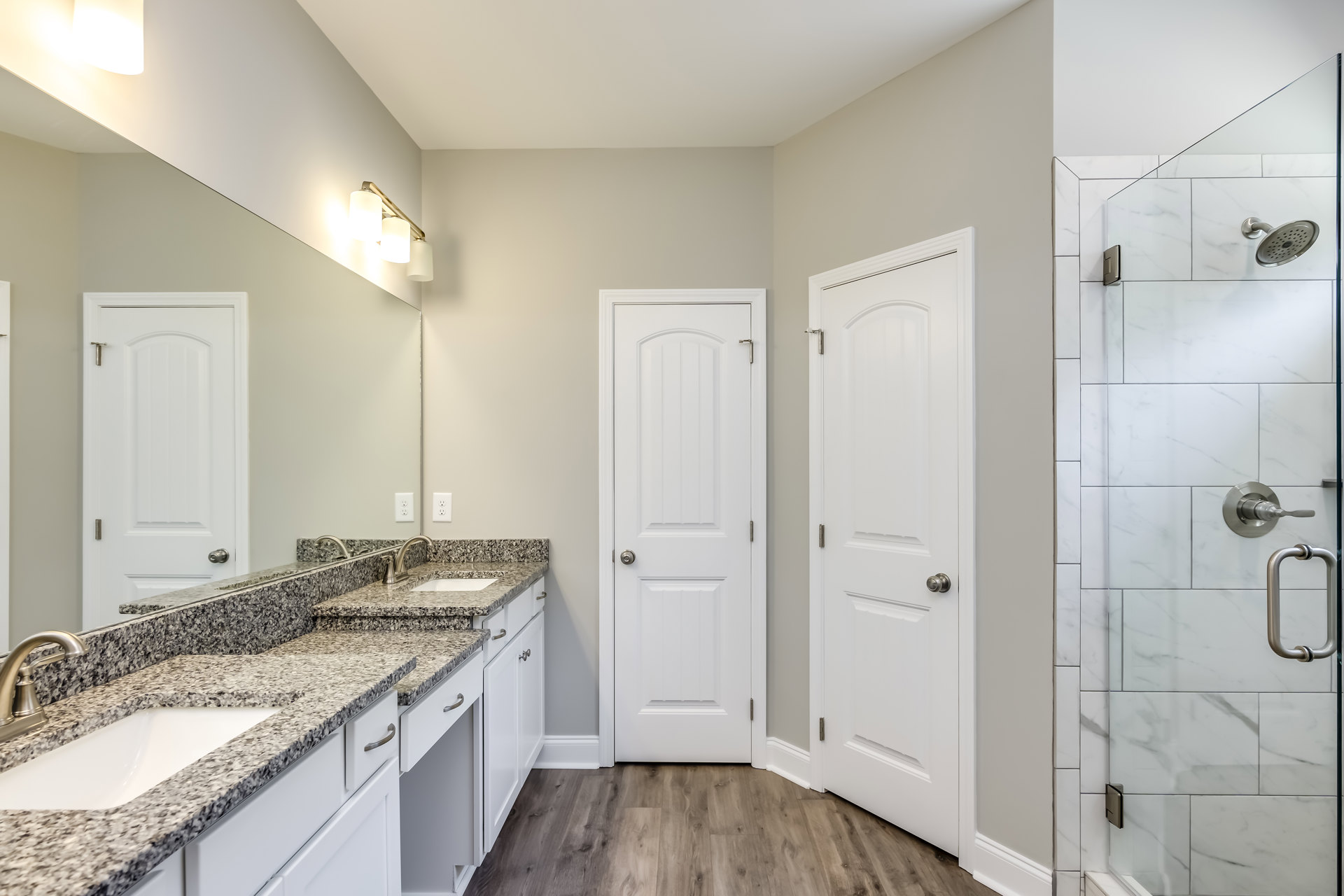 Bathroom featuring marble countertops, undermount sink with chrome faucet, glass-enclosed shower with metal handle, white cabinetry, and white door with silver knob