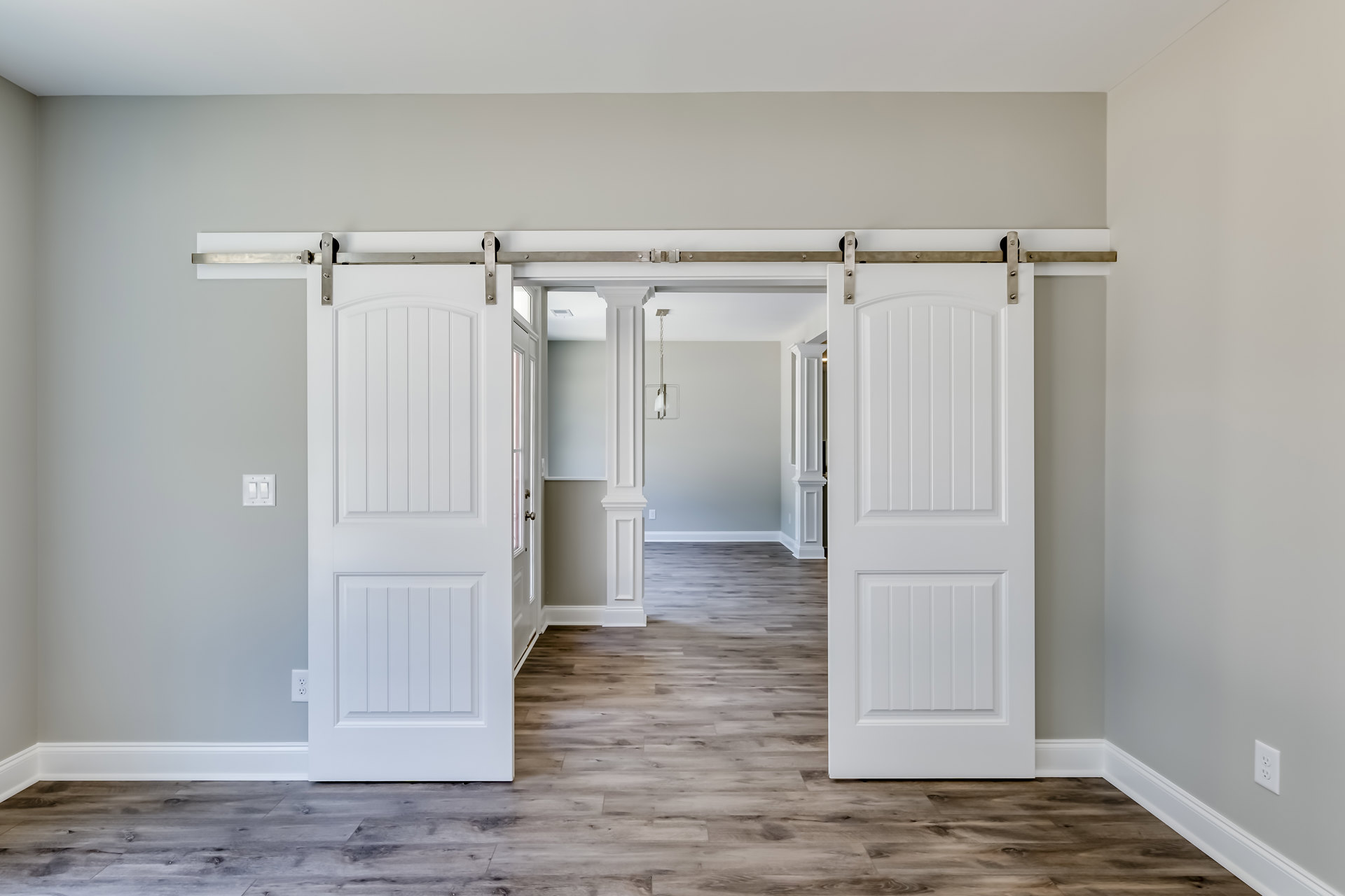 White sliding doors with vertical panels, wood flooring, white walls, and simple molding in a modern interior room.