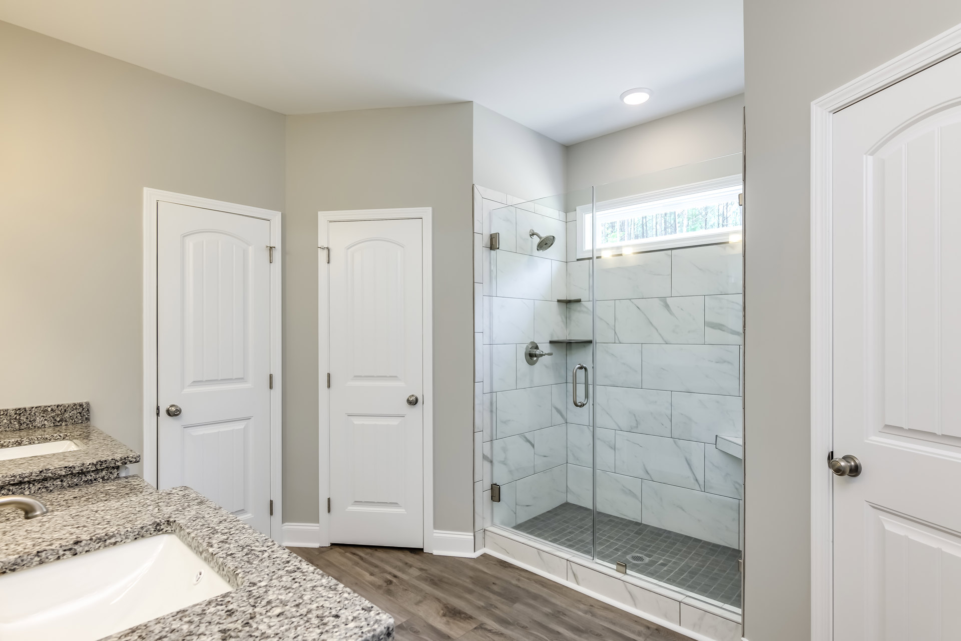 Modern bathroom featuring a glass shower enclosure, white tile walls, sleek sink with chrome faucet, white door with silver knob, and visible metal plumbing fixtures