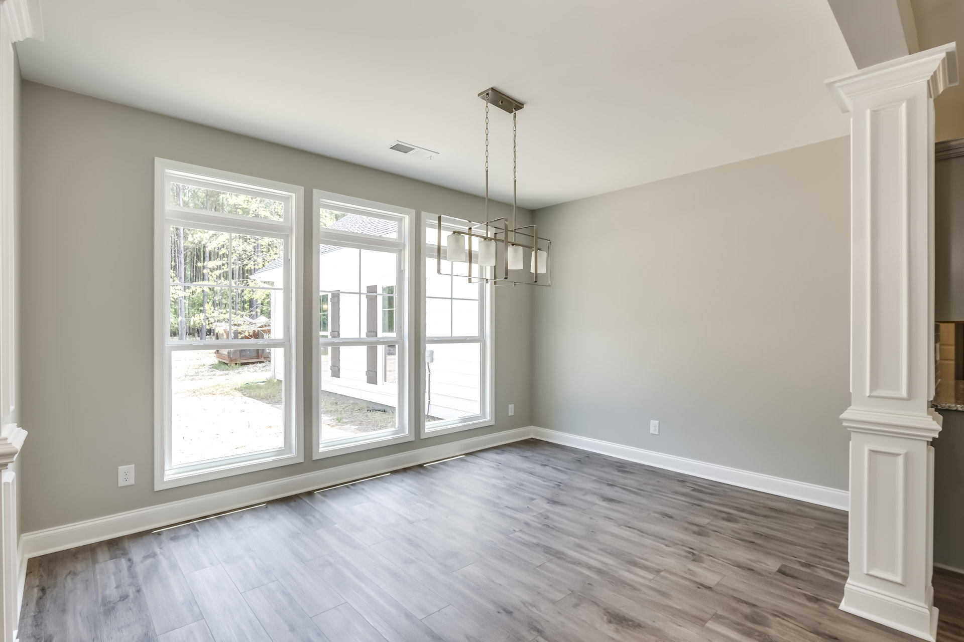 Sunlit room featuring wood flooring, large windows with views of trees, white door, and plaster walls with decorative molding