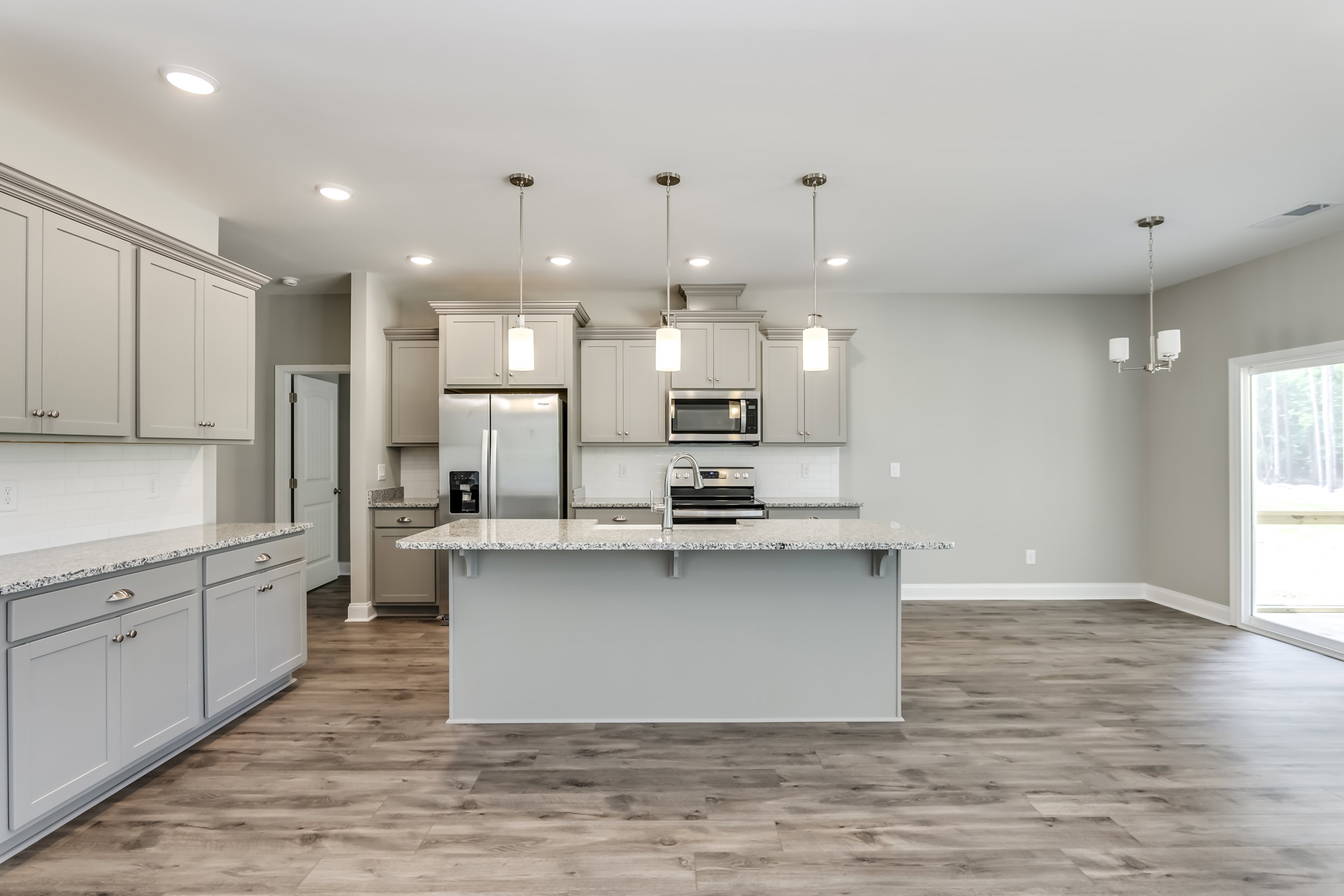 Spacious kitchen featuring a large central island with stone countertop, built-in sink and faucet, stainless steel refrigerator with water dispenser, white cabinetry, tile