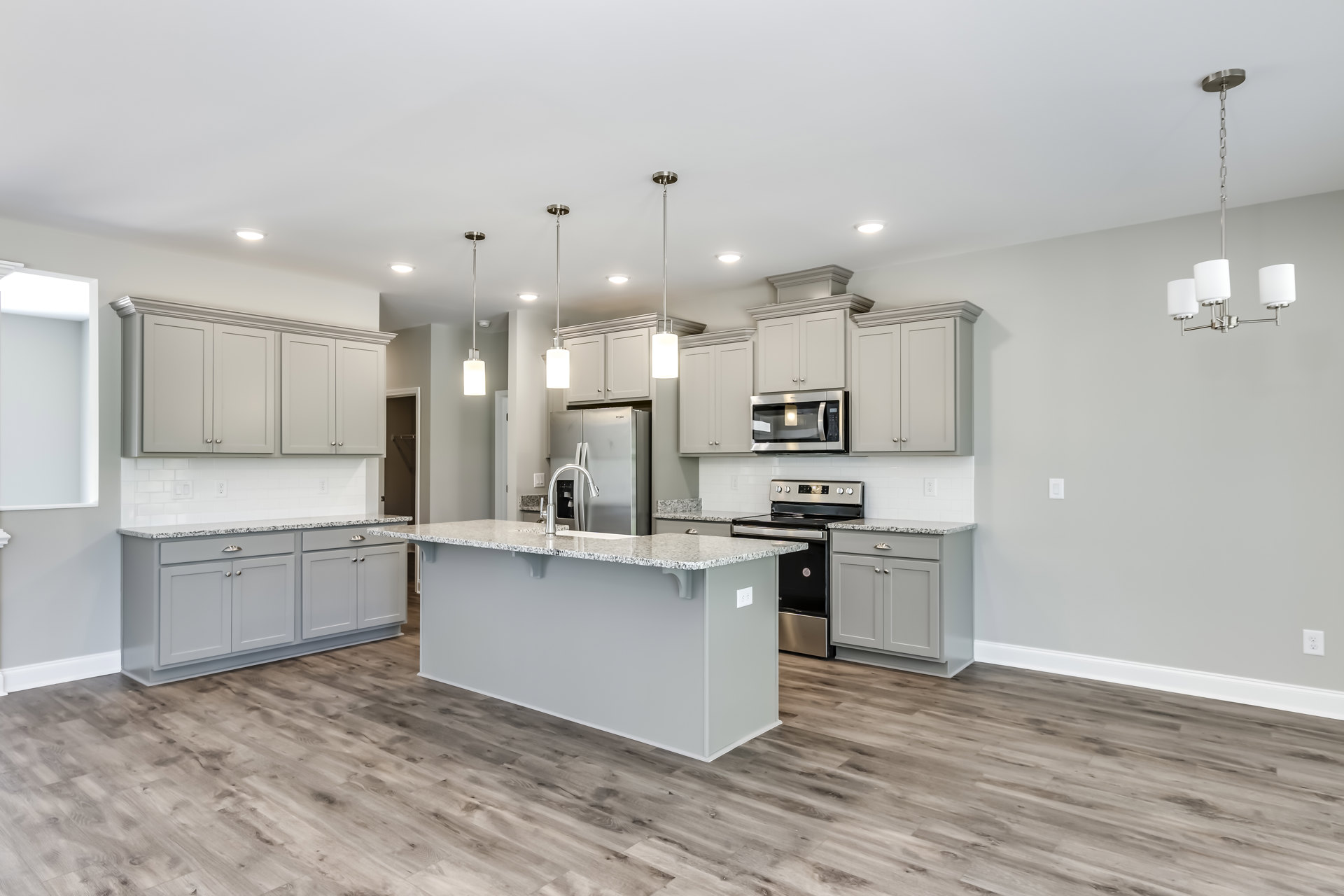 Spacious kitchen featuring a large marble island, stainless steel refrigerator, built-in microwave with illuminated window, white lamp shade, stove, and white cabinetry with stone