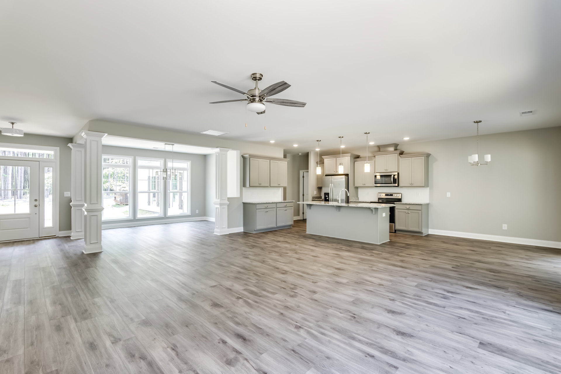 Spacious kitchen and dining area with hardwood floors, ceiling fan with light, white plaster walls, wood cabinetry, and kitchen counter featuring a stainless steel sink