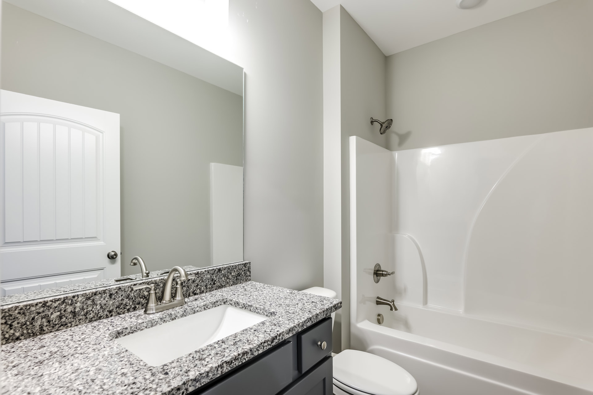 Bathroom with white tile walls, built-in bathtub, modern sink with chrome faucet, white toilet, and wall-mounted shower head.