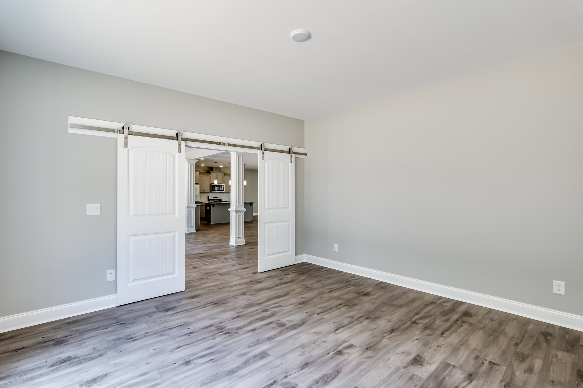 Sliding white door with wood laminate flooring, white plaster walls, and minimalist interior design.