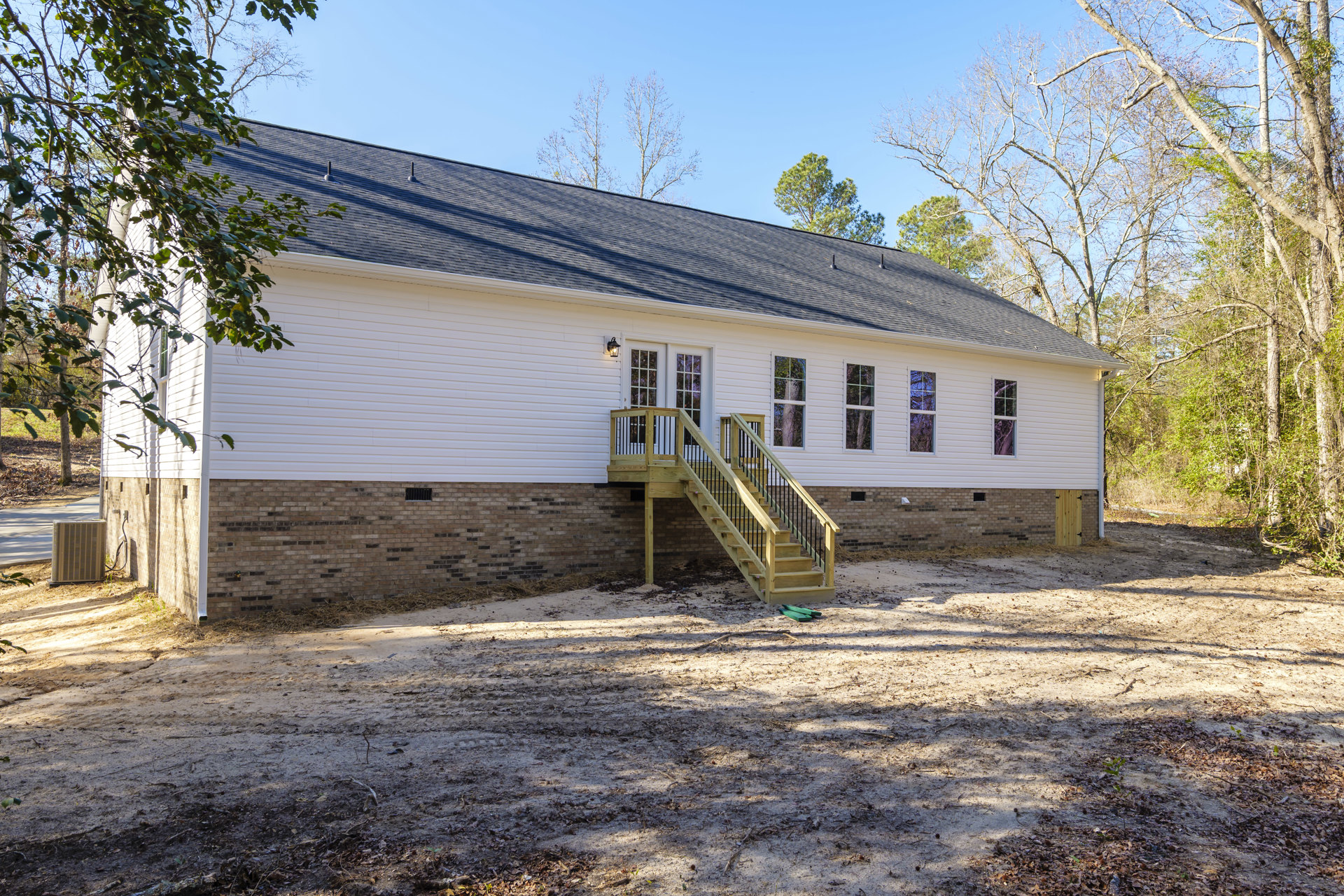 White exterior home with wooden staircase leading to entry, large metal utility box on ground, brick accents, windows, and surrounding greenery.