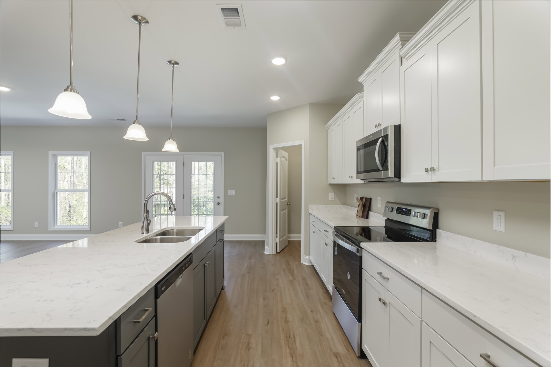 White kitchen cabinets, black appliances including an open microwave, stainless steel sink and faucet on a light countertop, window with trees visible outside.