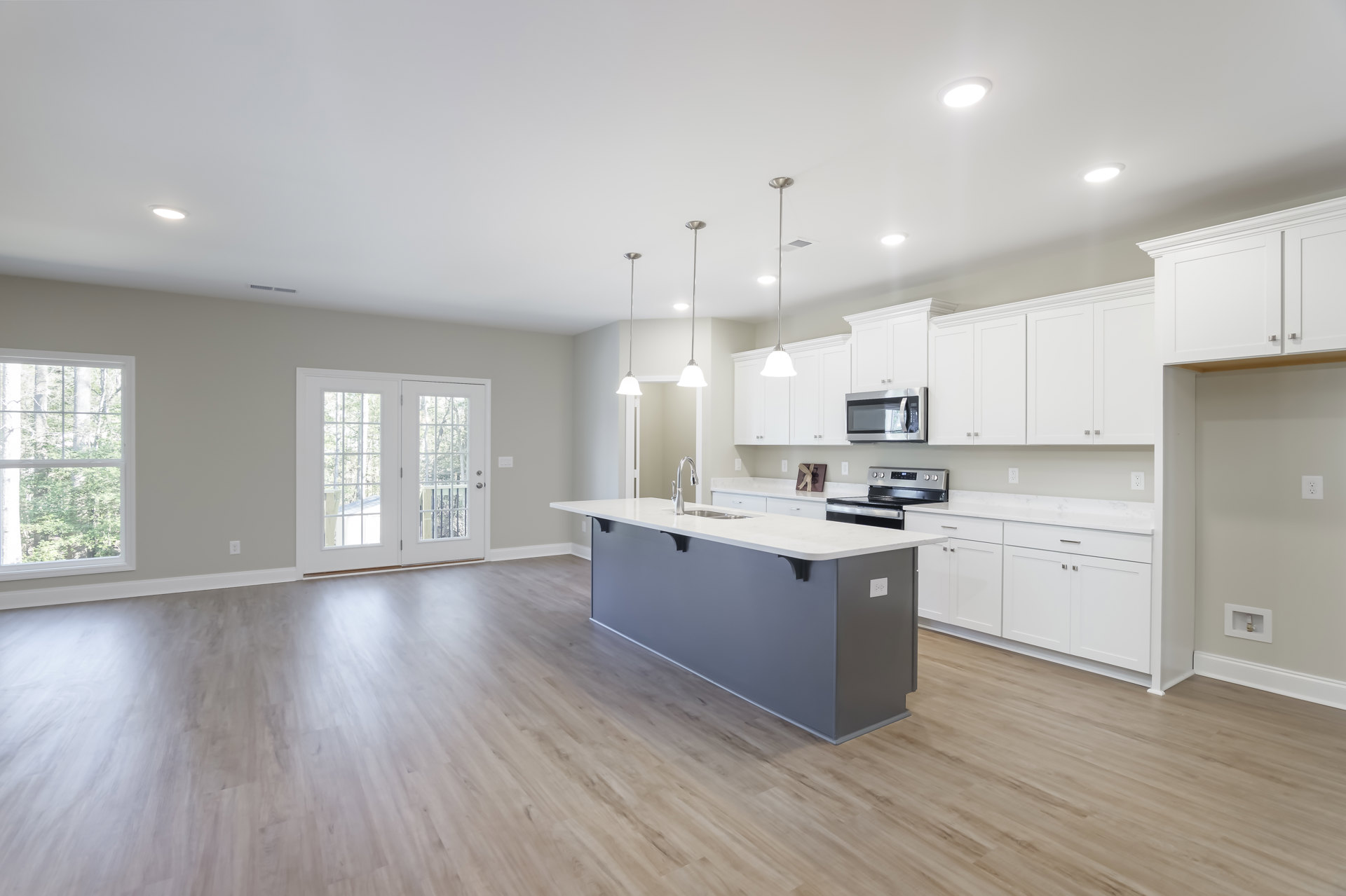 White cabinetry kitchen featuring a spacious island with built-in sink and stove, stainless steel microwave, glass-paneled double doors, ceiling light fixture, and window