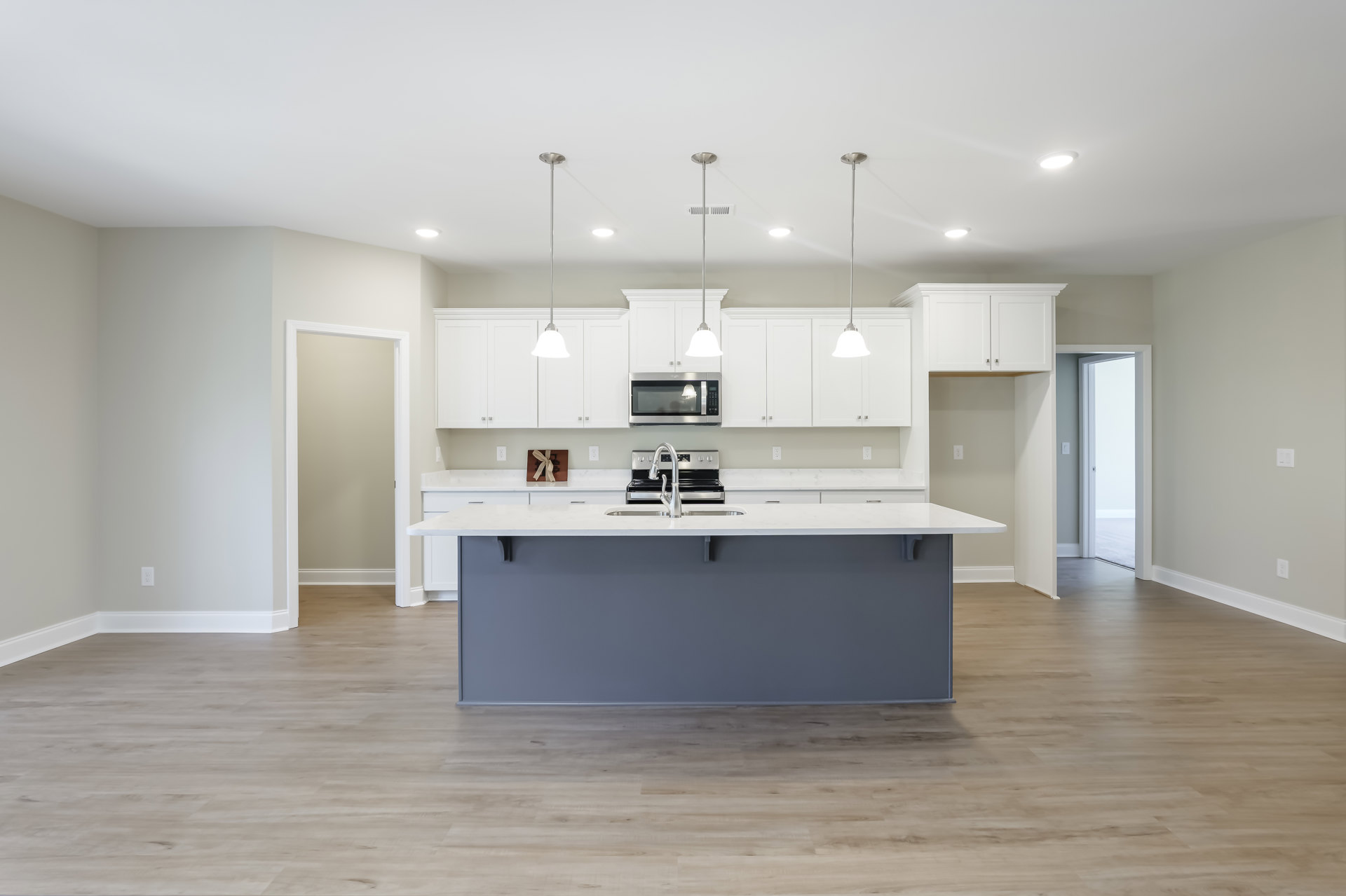 Kitchen with white shaker cabinets, central island with quartz countertop, stainless steel appliances, undermount sink, modern faucet, light hardwood flooring, recessed lighting