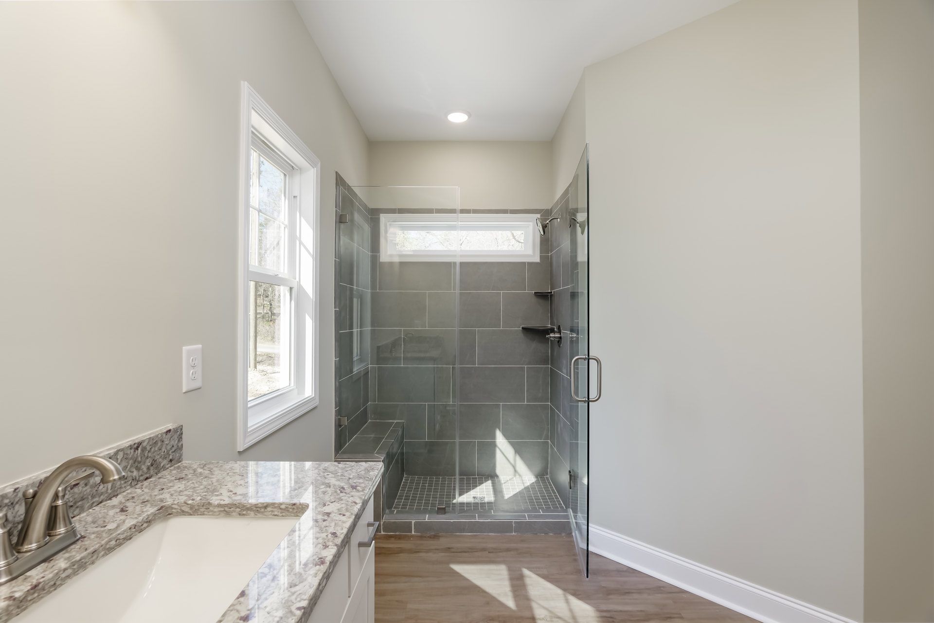 Modern bathroom featuring a glass-enclosed shower, white tile walls, sleek sink with chrome faucet, and a window overlooking leafy trees
