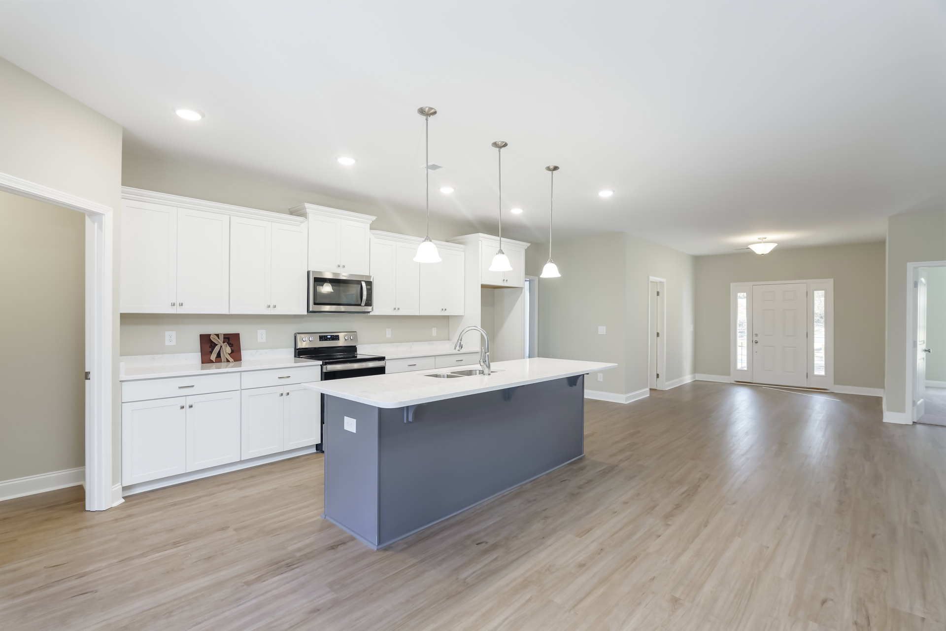 White cabinetry kitchen featuring a spacious island with built-in sink, stainless steel microwave, glass-paneled door, and light-colored countertops.