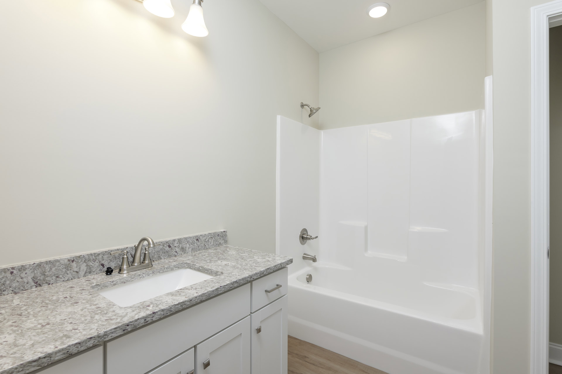 White bathtub with chrome faucet beside a tiled wall, light wood vanity with undermount sink and silver tap, stone countertop, and modern cabinetry in a bright bathroom.