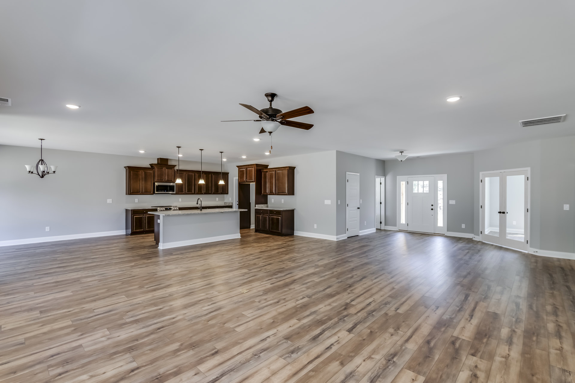 Spacious open floor plan featuring hardwood flooring, kitchen island with white cabinetry, adjacent dining area, recessed lighting, and white doors with black hardware and glass