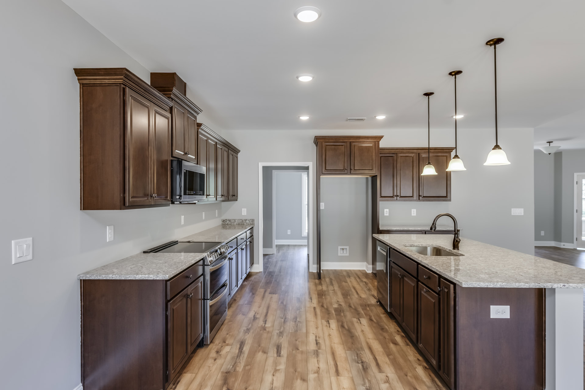 Dark wood kitchen cabinets with granite countertops, stainless steel microwave mounted on the wall, white wall with visible hole and light switch, pole with attached light fixture