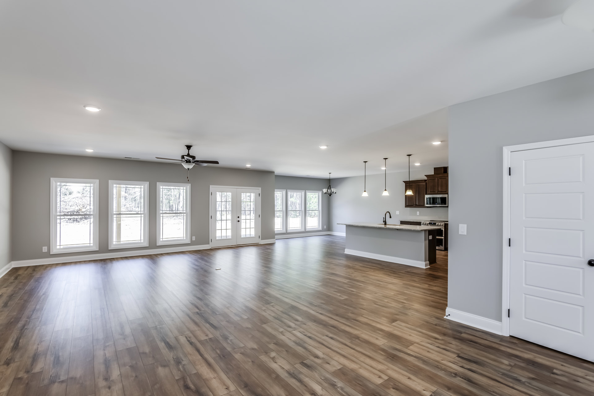 Spacious open floor plan featuring wood flooring, modern kitchen with white cabinetry and black hardware, dining area, large windows showcasing snowy forest views