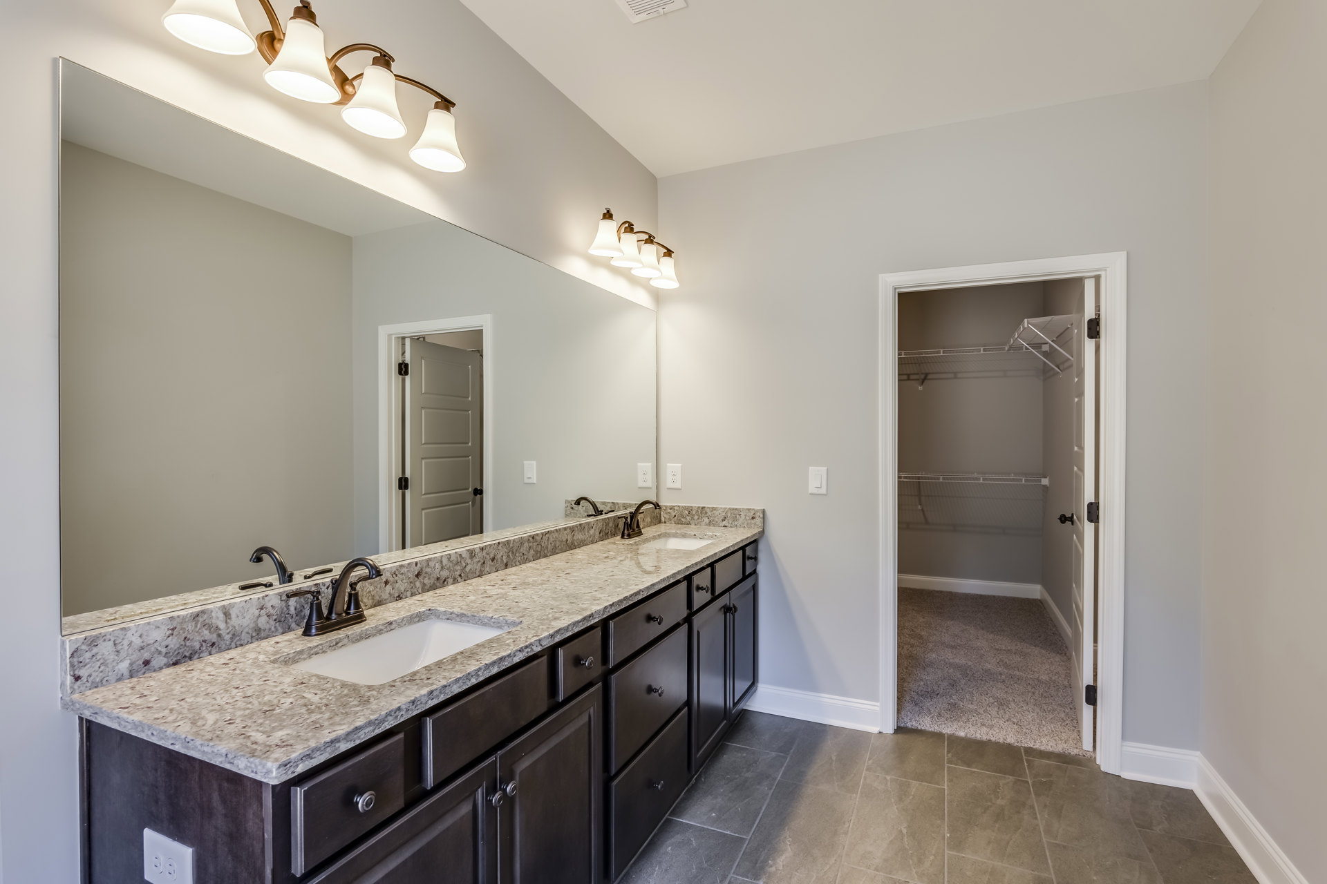 Bathroom with double vanity featuring white sinks, chrome faucets, large wall mirror, light gray tile backsplash, white cabinetry, and quartz countertop