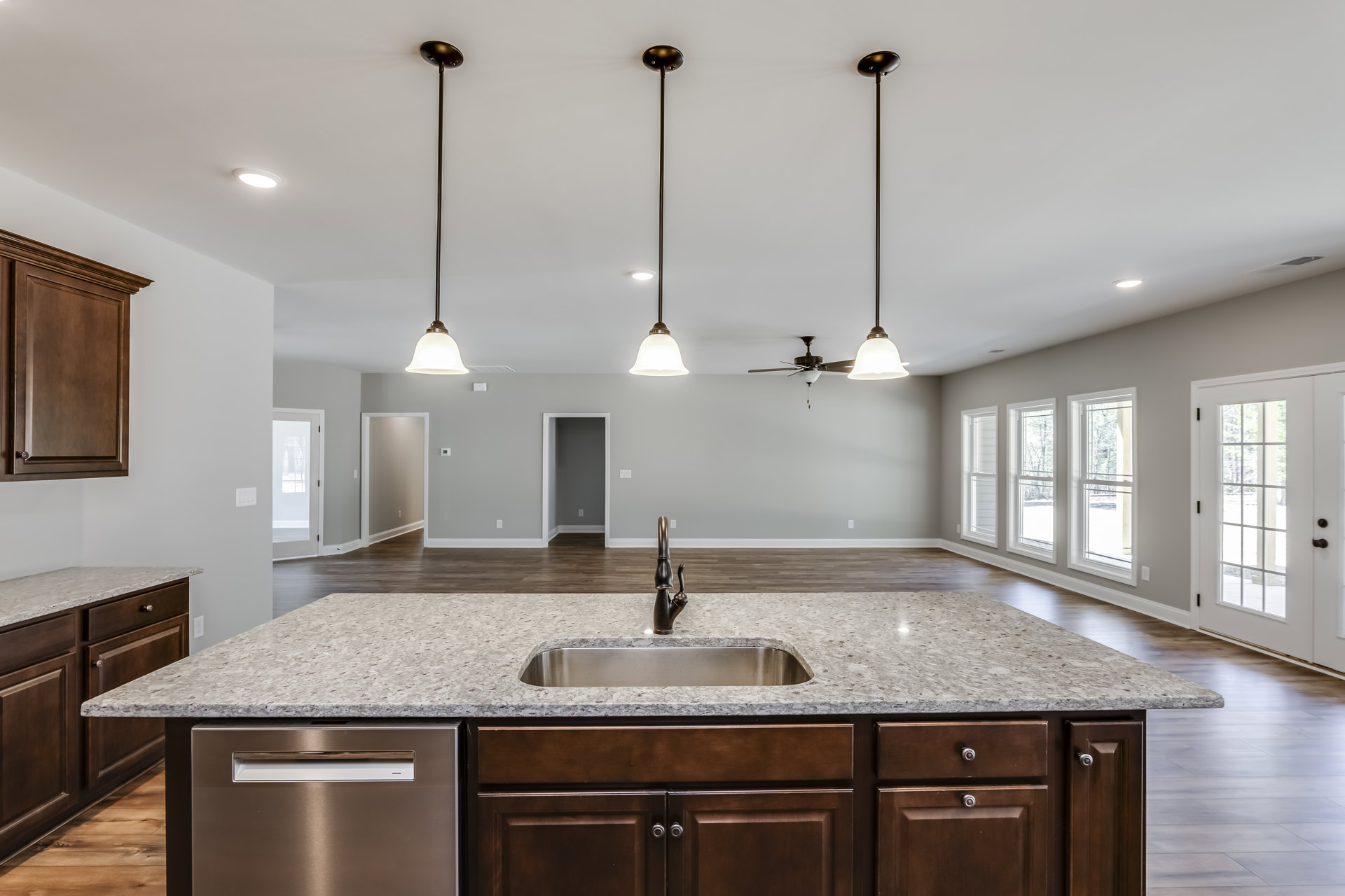 Granite countertop kitchen with stainless steel sink, white cabinetry, tile backsplash, ceiling fan, glass-paneled door, and built-in dishwasher