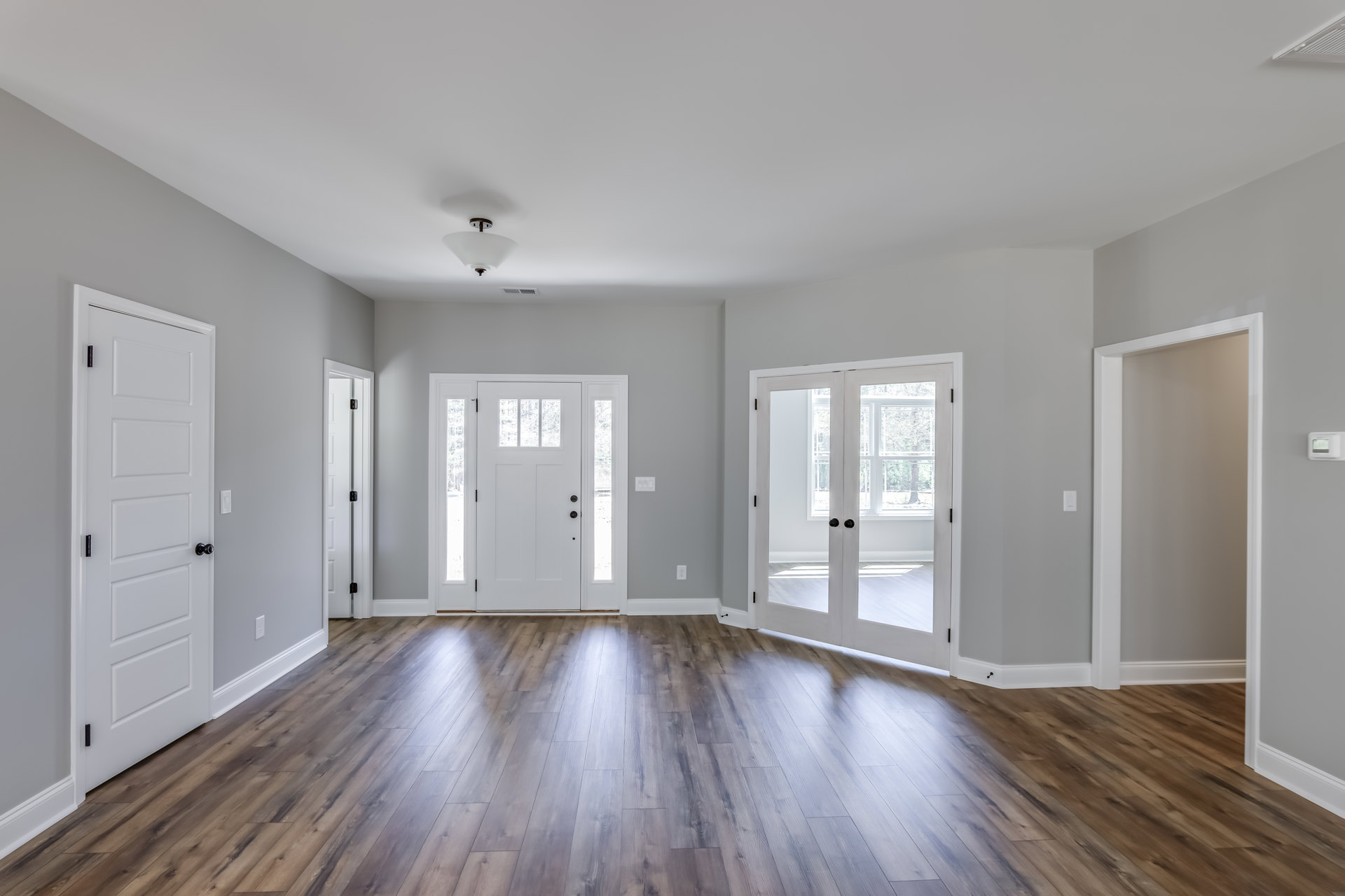 White double doors with black knobs set against white walls, wood laminate flooring throughout, minimal interior detailing.