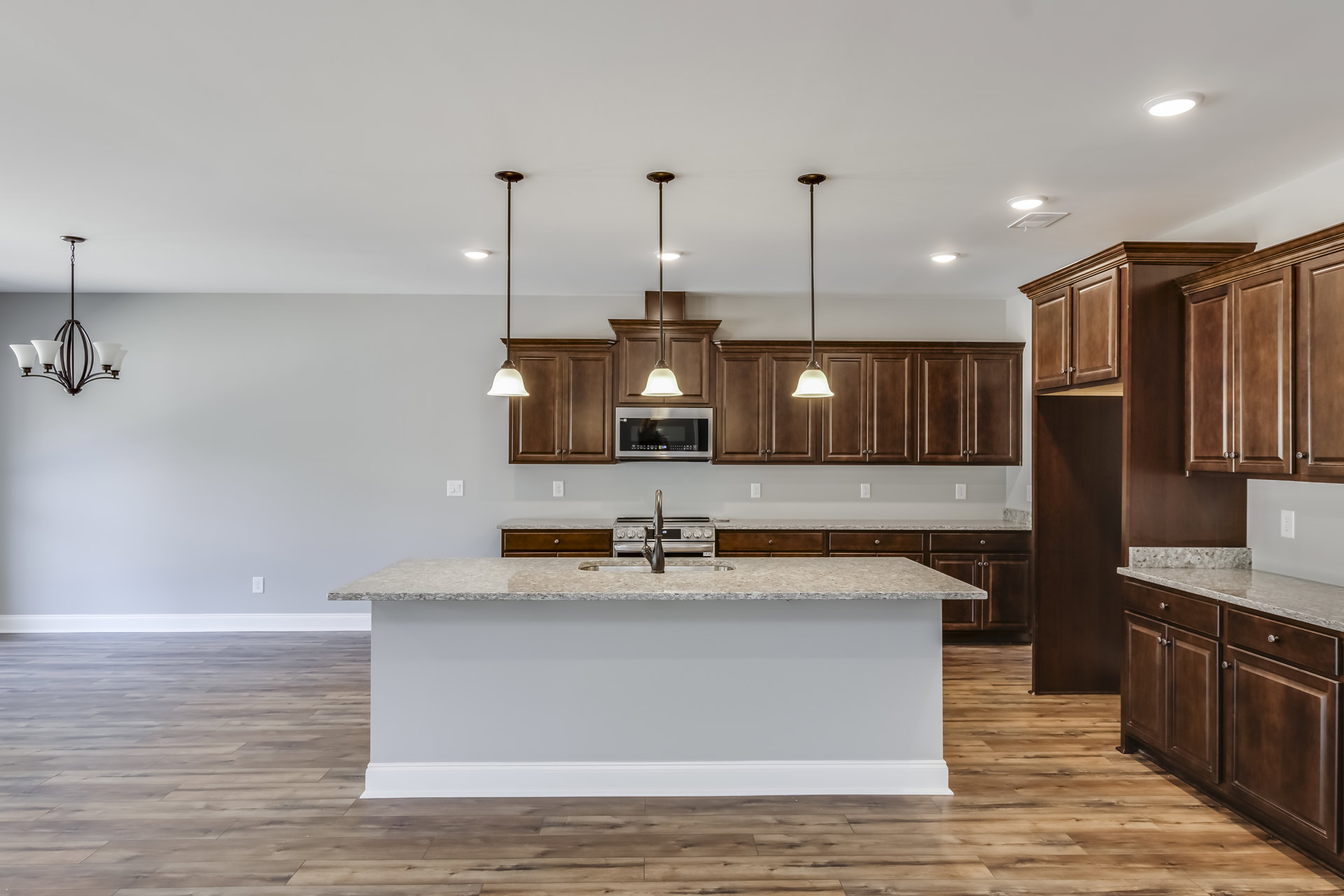 Spacious kitchen featuring a large granite island with built-in sink, white cabinetry, tile flooring, stainless steel microwave reflecting a person, bell-shaped pendant light