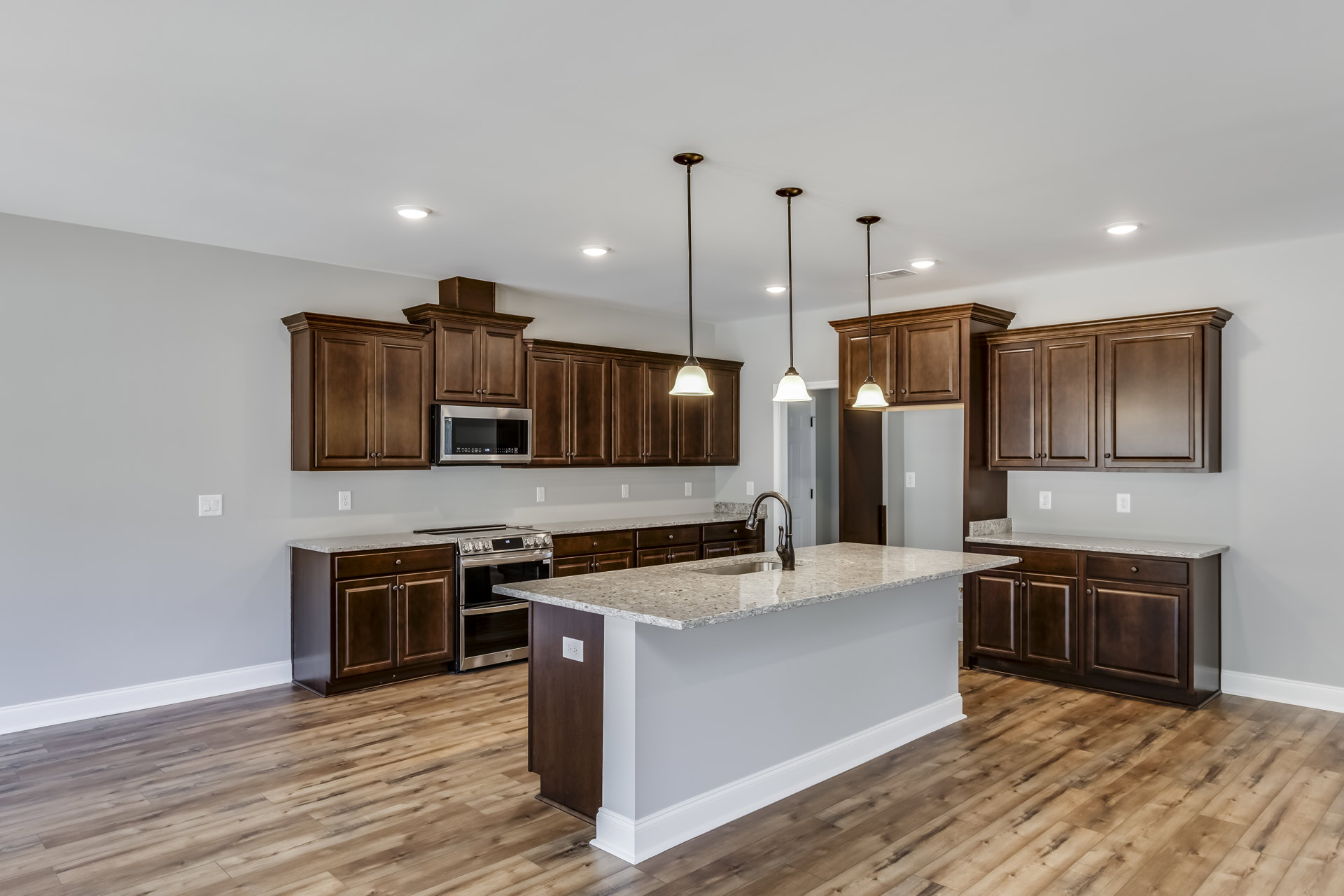 Spacious kitchen featuring a large central island with built-in sink, white cabinetry, stone countertops, stainless steel stove, microwave with digital display, and recessed