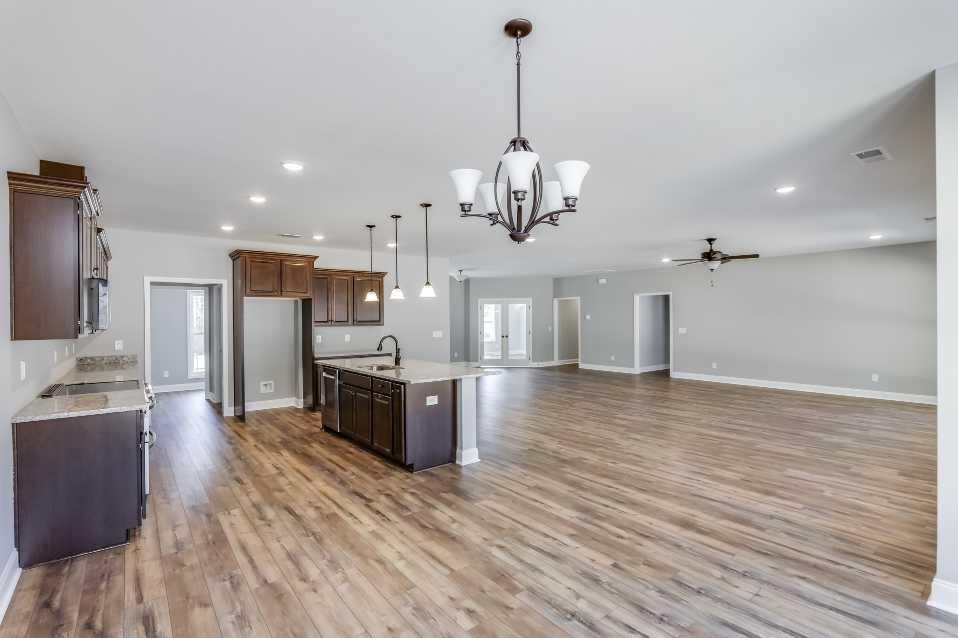 Spacious open-concept kitchen featuring a central island with sink, hardwood flooring, white cabinetry, glass-paneled double doors, and modern appliances