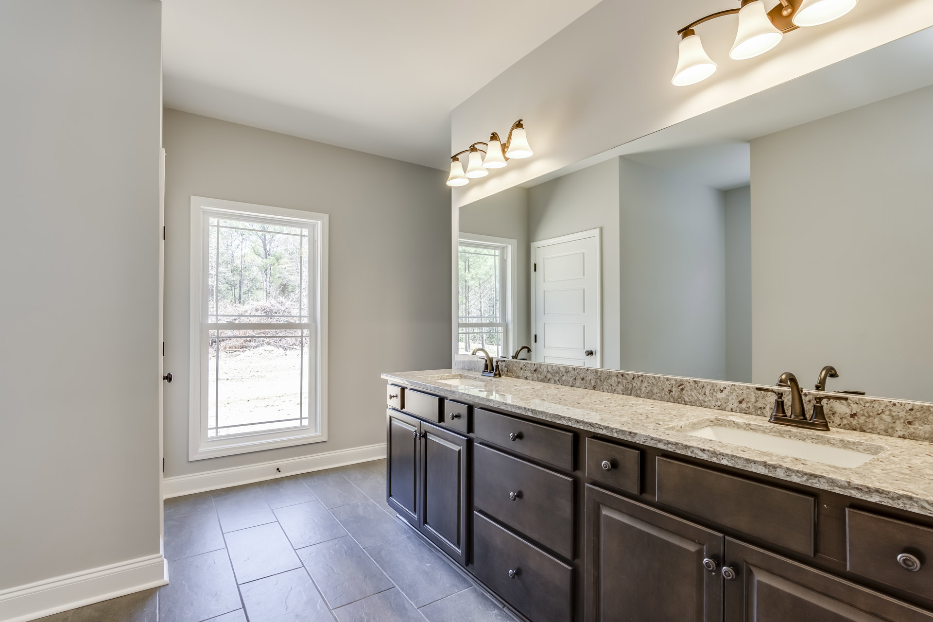 Bathroom with double vanity featuring white sinks, marble countertop, large framed mirror, gold faucet and hardware, light fixture with four bulbs above mirror, white cabinetry