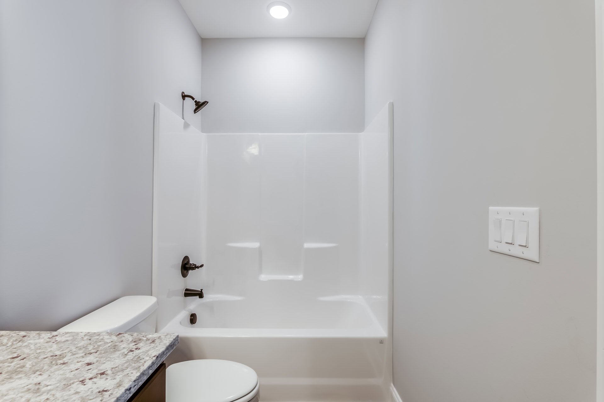 Bathroom with white tile walls, built-in bathtub, white toilet, chrome shower head, and light-colored countertop