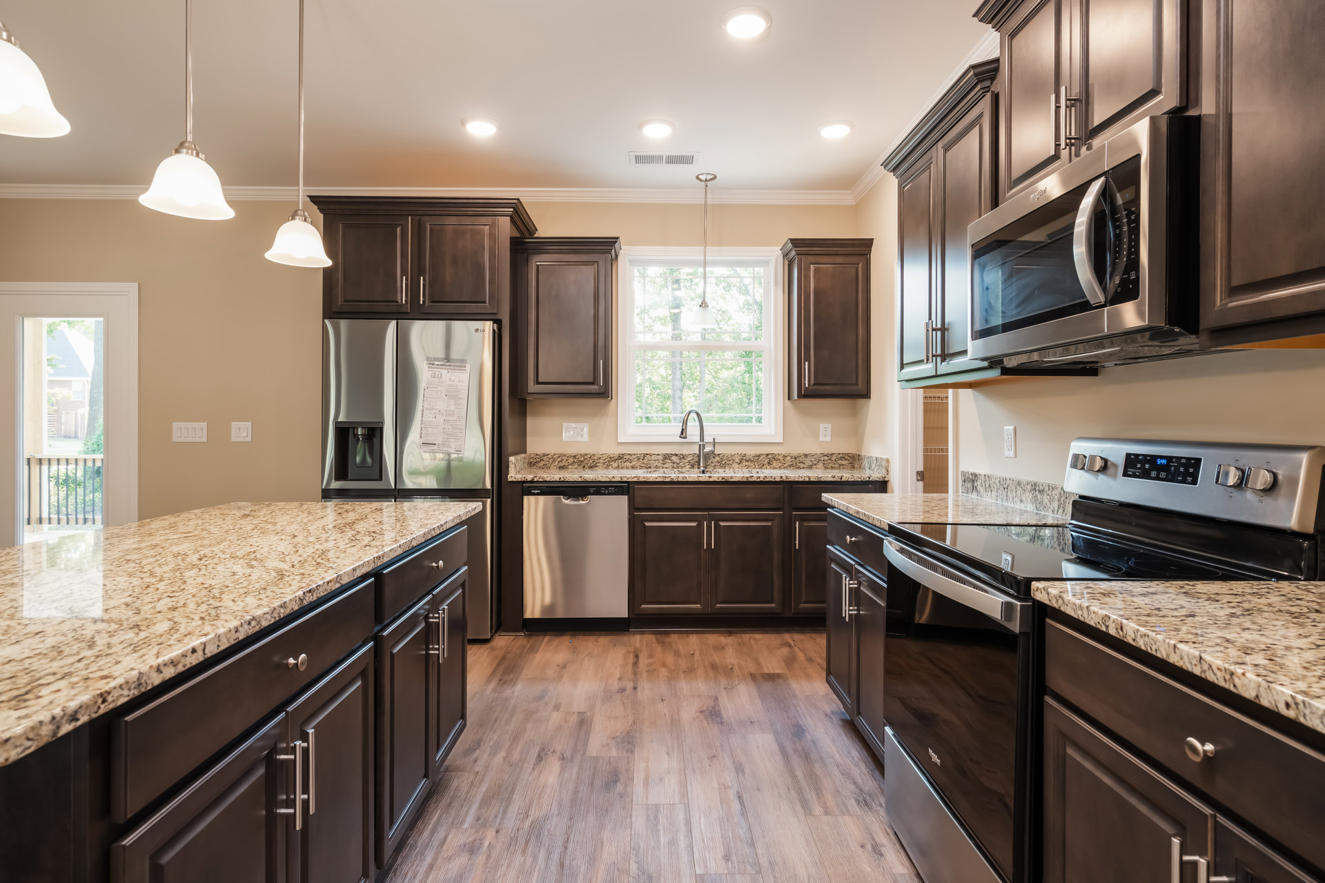 Granite countertops, stainless steel appliances, white cabinetry, built-in microwave, window above sink with pendant light, close-up views of stove, dishwasher, and door