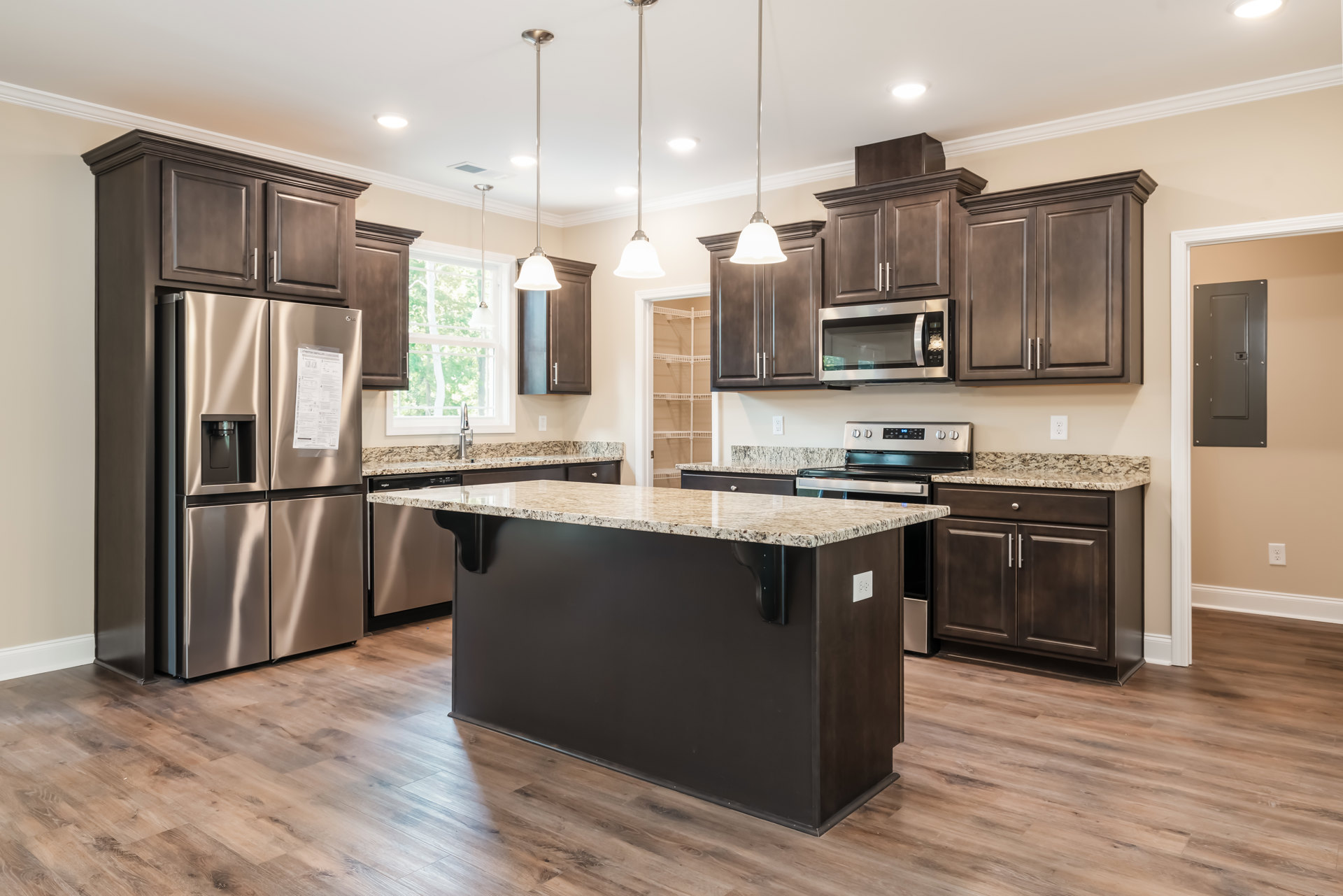 Kitchen with granite countertops, central island, stainless steel refrigerator with paper attached, built-in microwave, grey door with square handle, white sign with black text