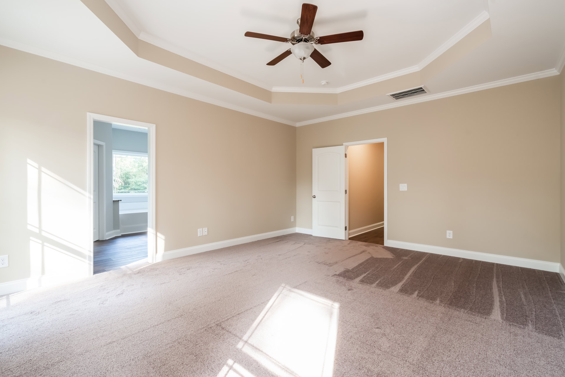 Bedroom with plush white carpet, ceiling fan with light fixture, white walls, and a closed white door with silver knob