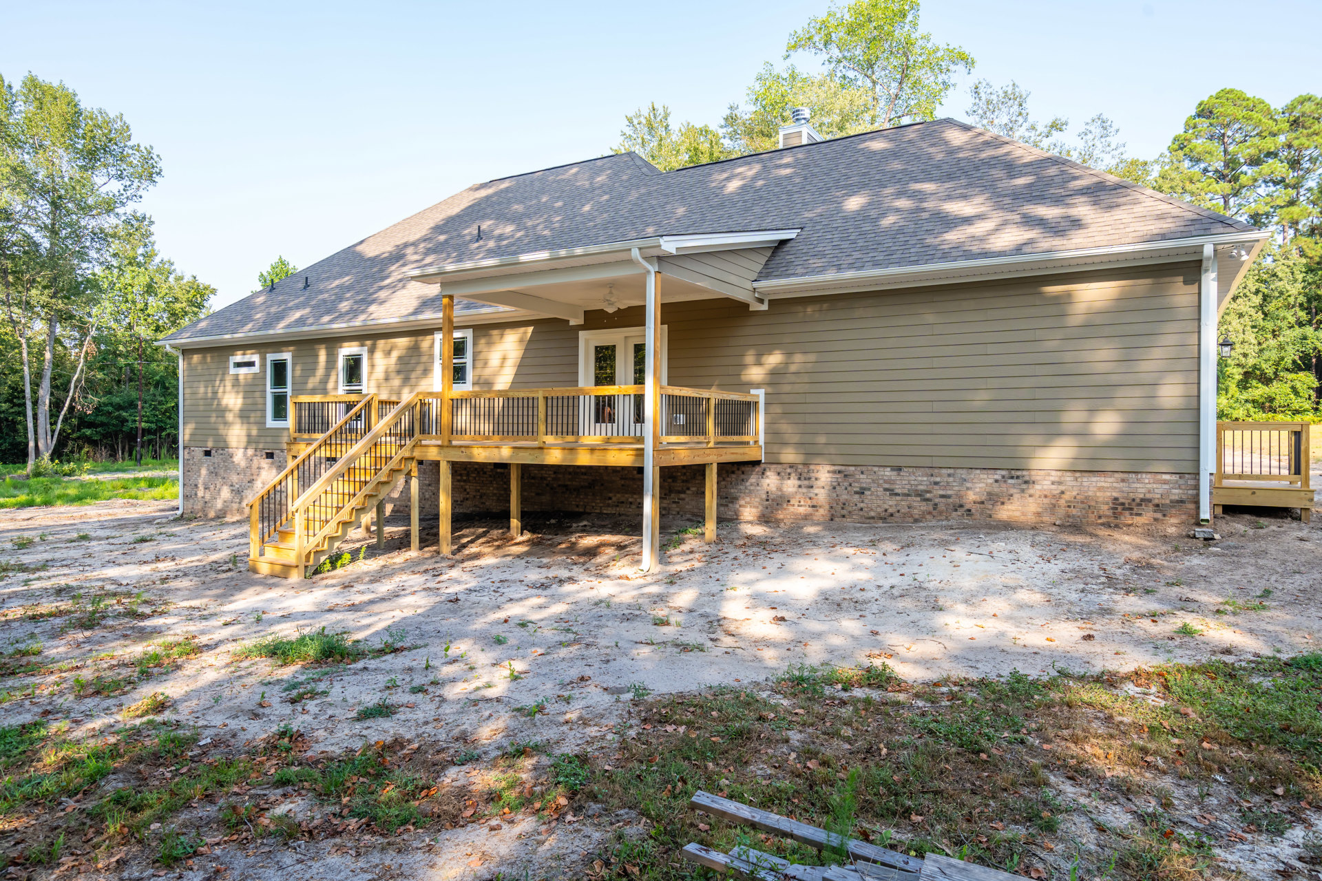 Wooden porch with railing and stairs leading to entry, surrounded by trees and plants, cottage-style exterior with natural finishes