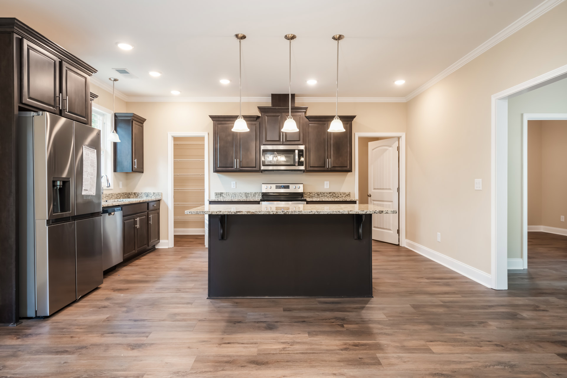 Spacious kitchen featuring a large marble-topped island, stainless steel refrigerator with a paper attached, dark cabinetry, blurred microwave, white support pole on the island