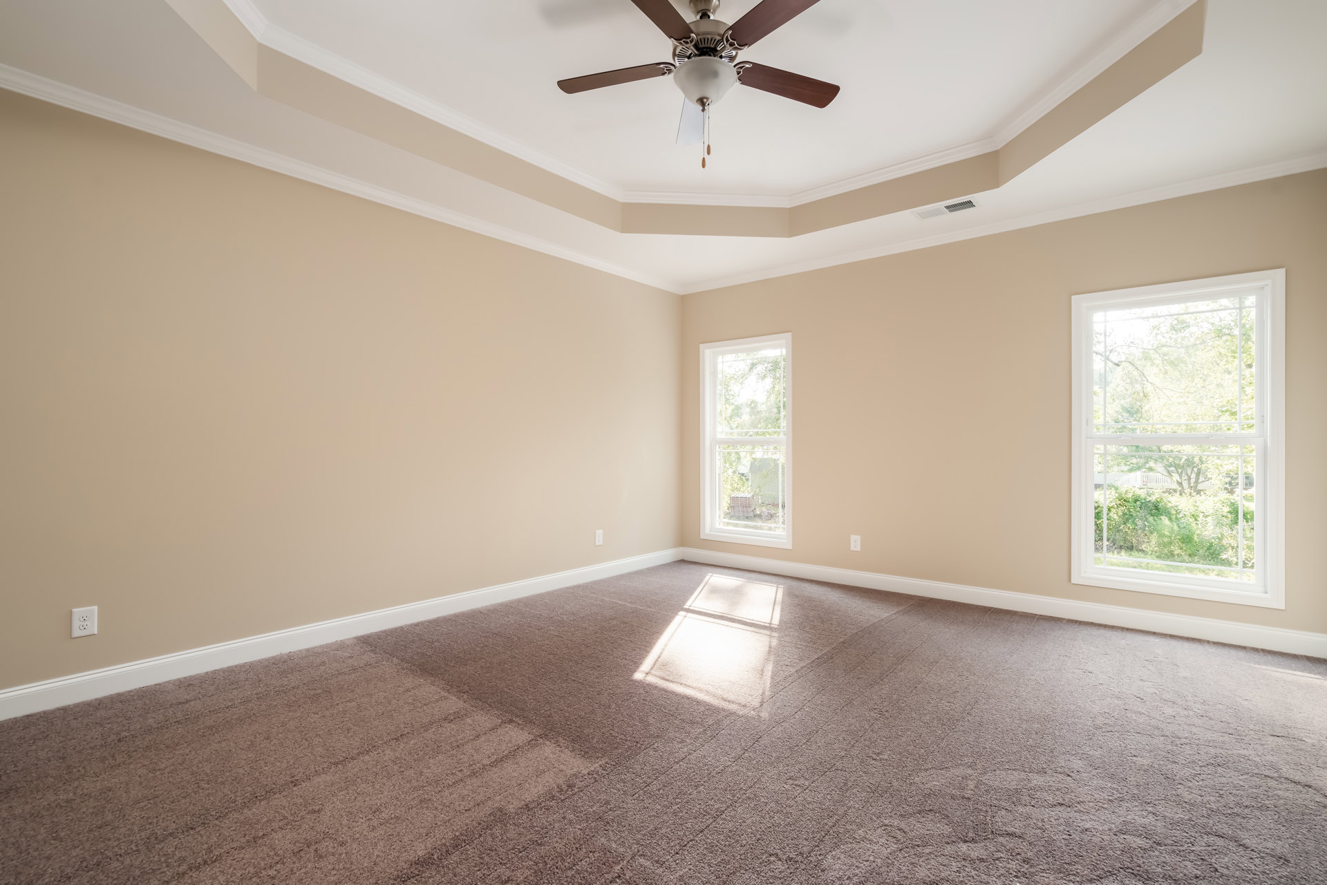 Neutral-toned room with white carpet, square window overlooking trees, ceiling fan with light fixture, plaster walls, and crown molding.