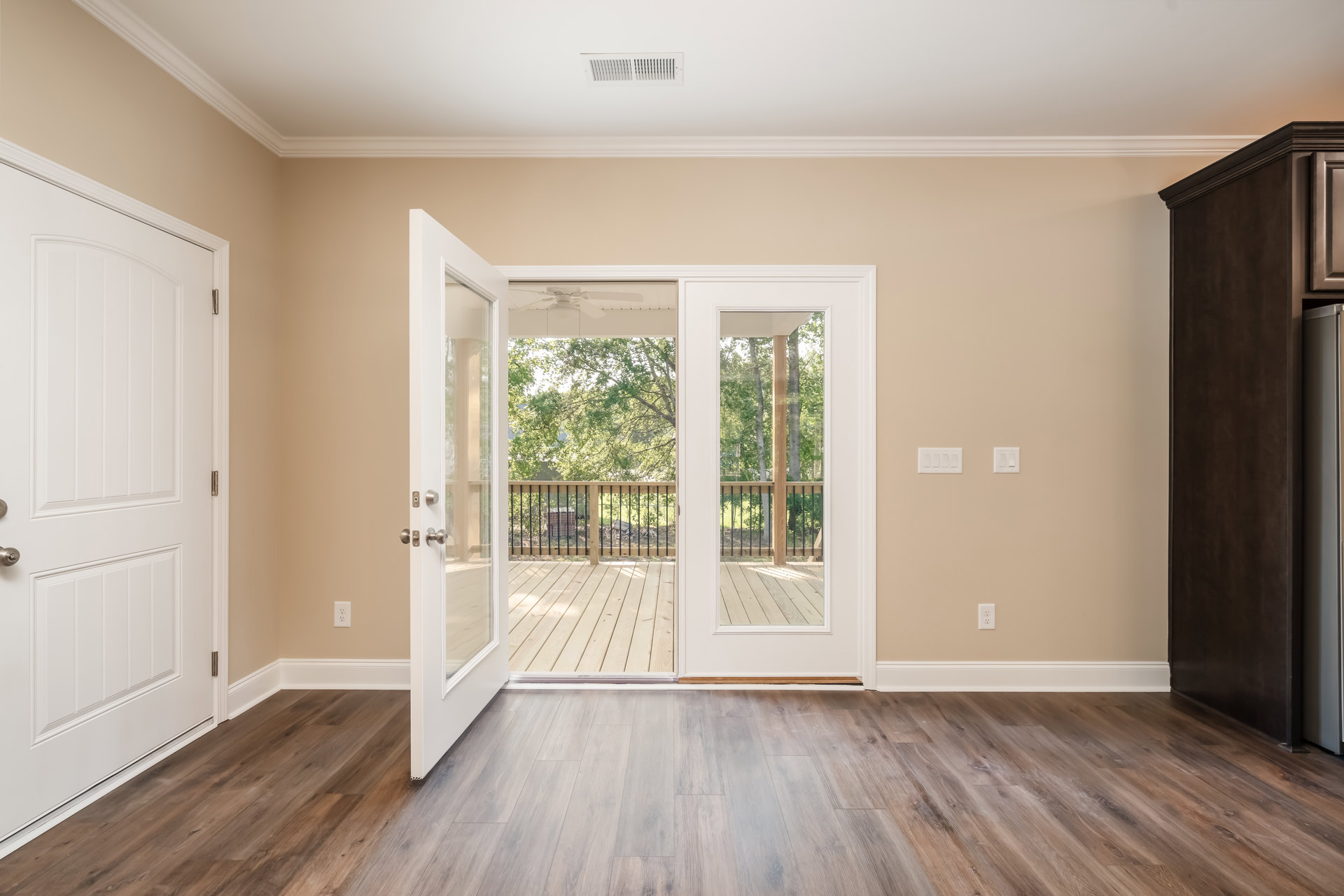 Wood floor with white trim, white door featuring silver hardware, sliding glass door opening to deck with trees visible outside.