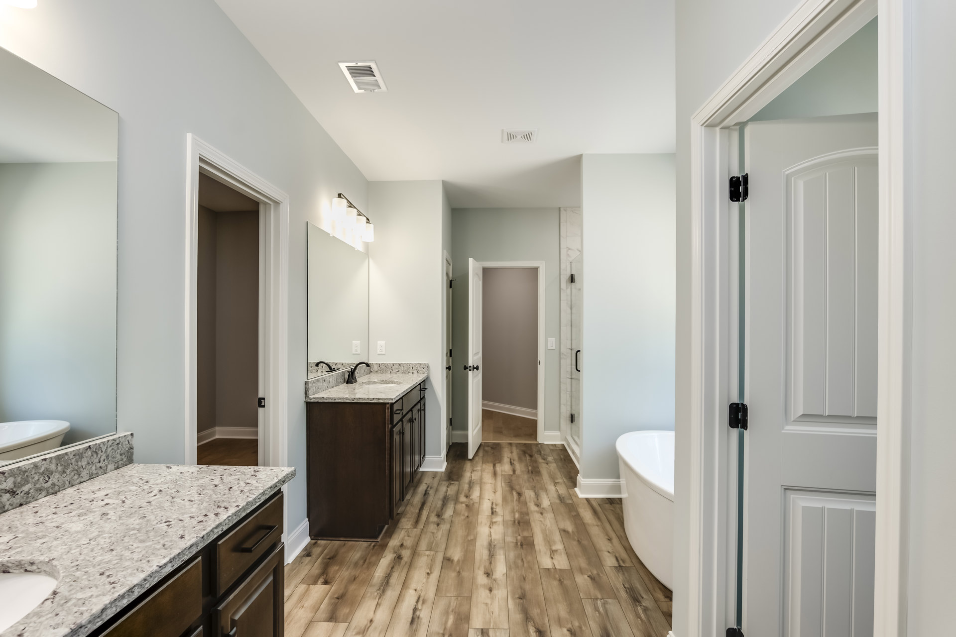 Bathroom with freestanding white bathtub, rectangular sink set in marble countertop, wood flooring, white walls, ceiling vent, and modern cabinetry