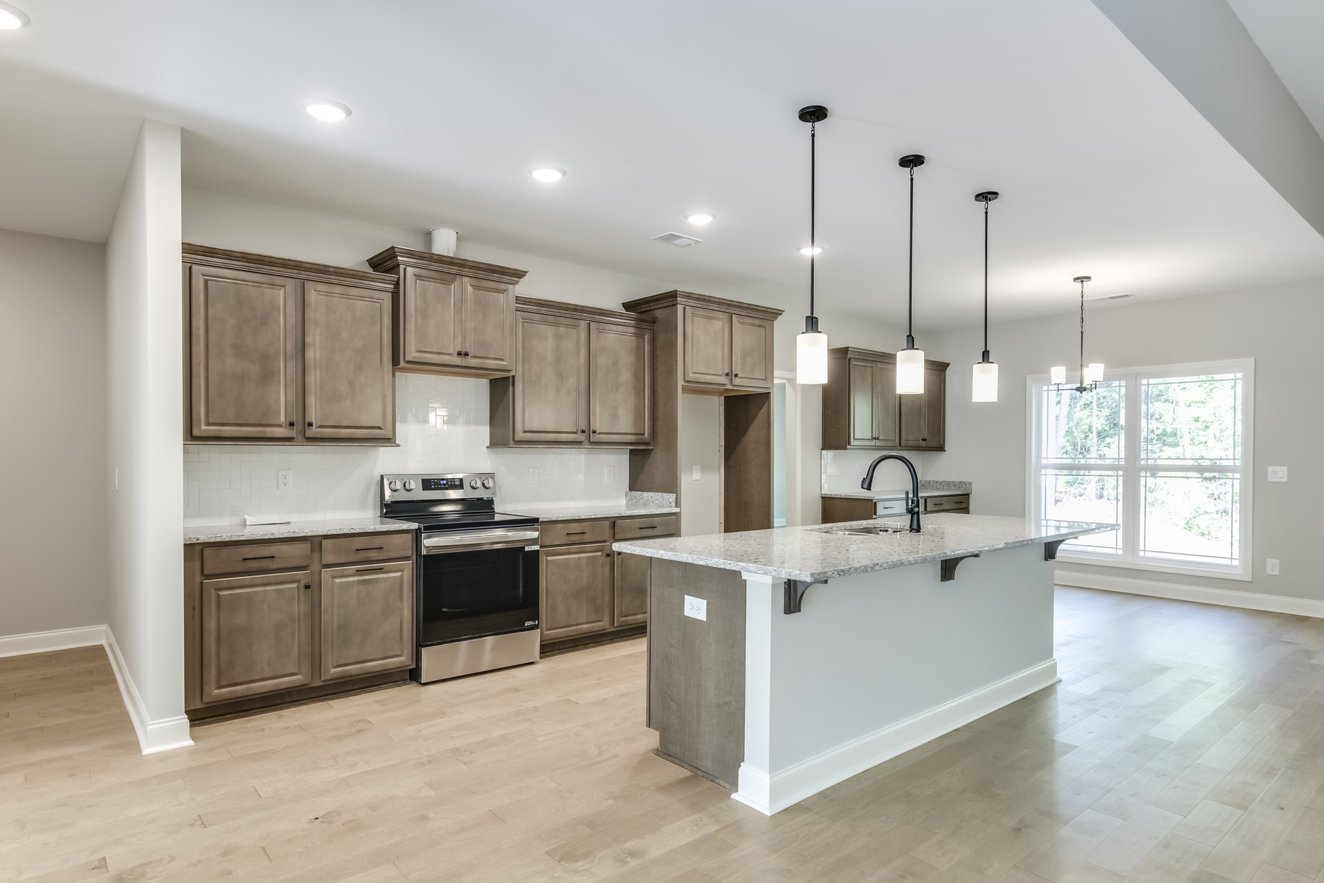 Modern kitchen featuring a marble island with built-in sink, stainless steel stove and oven, white cabinetry, large window, and hardwood flooring