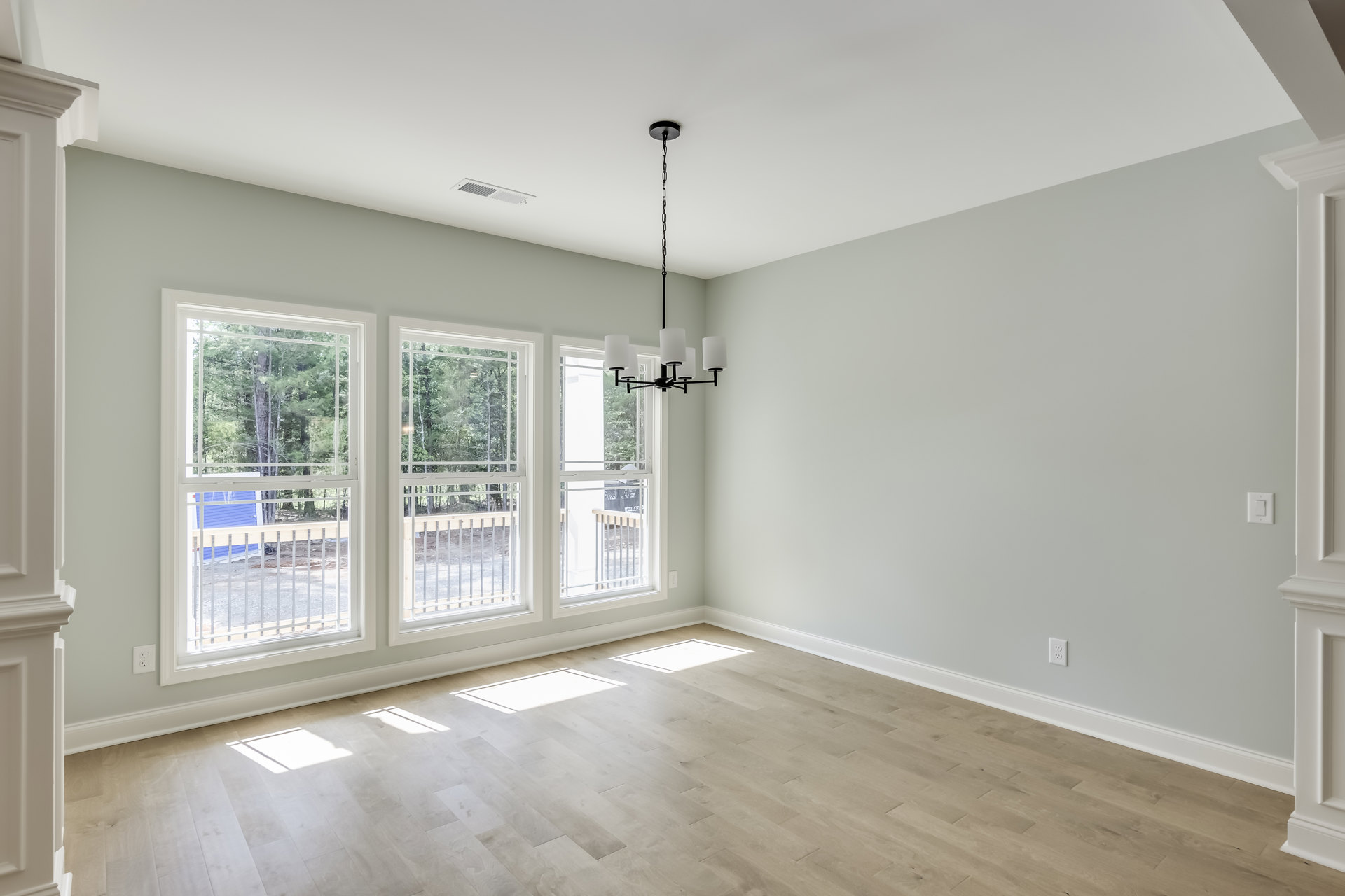 Open room with white walls, wooden floor, large windows, and a central chandelier