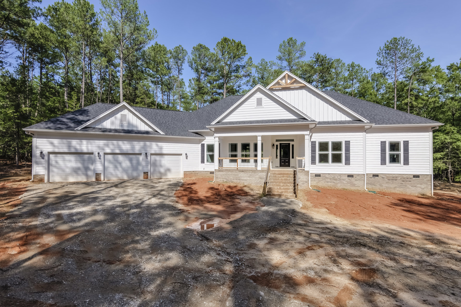 Two-story home with black front door, white-framed windows, covered porch, paved driveway, and mature trees behind the house