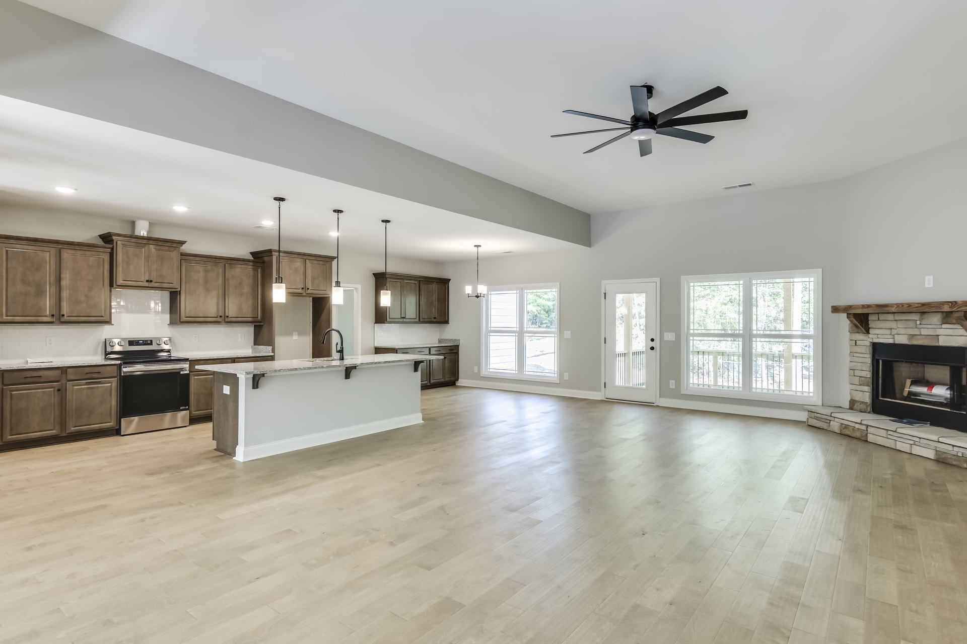 Spacious open floor plan featuring a central kitchen island with stone countertop and built-in sink, stainless steel stove and oven, white cabinetry, ceiling fan with light