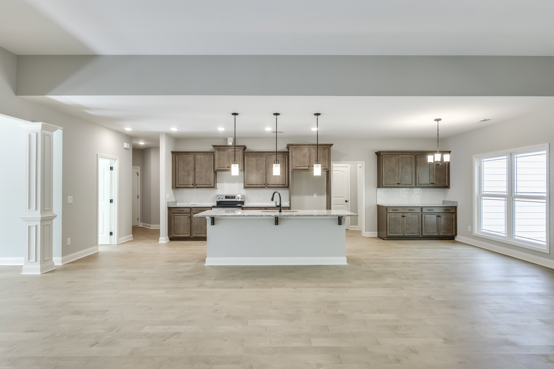 Open kitchen and dining area featuring a large central island with built-in sink, wood flooring, white walls, floating shelf, white-framed window, and wall-mounted light fixture.