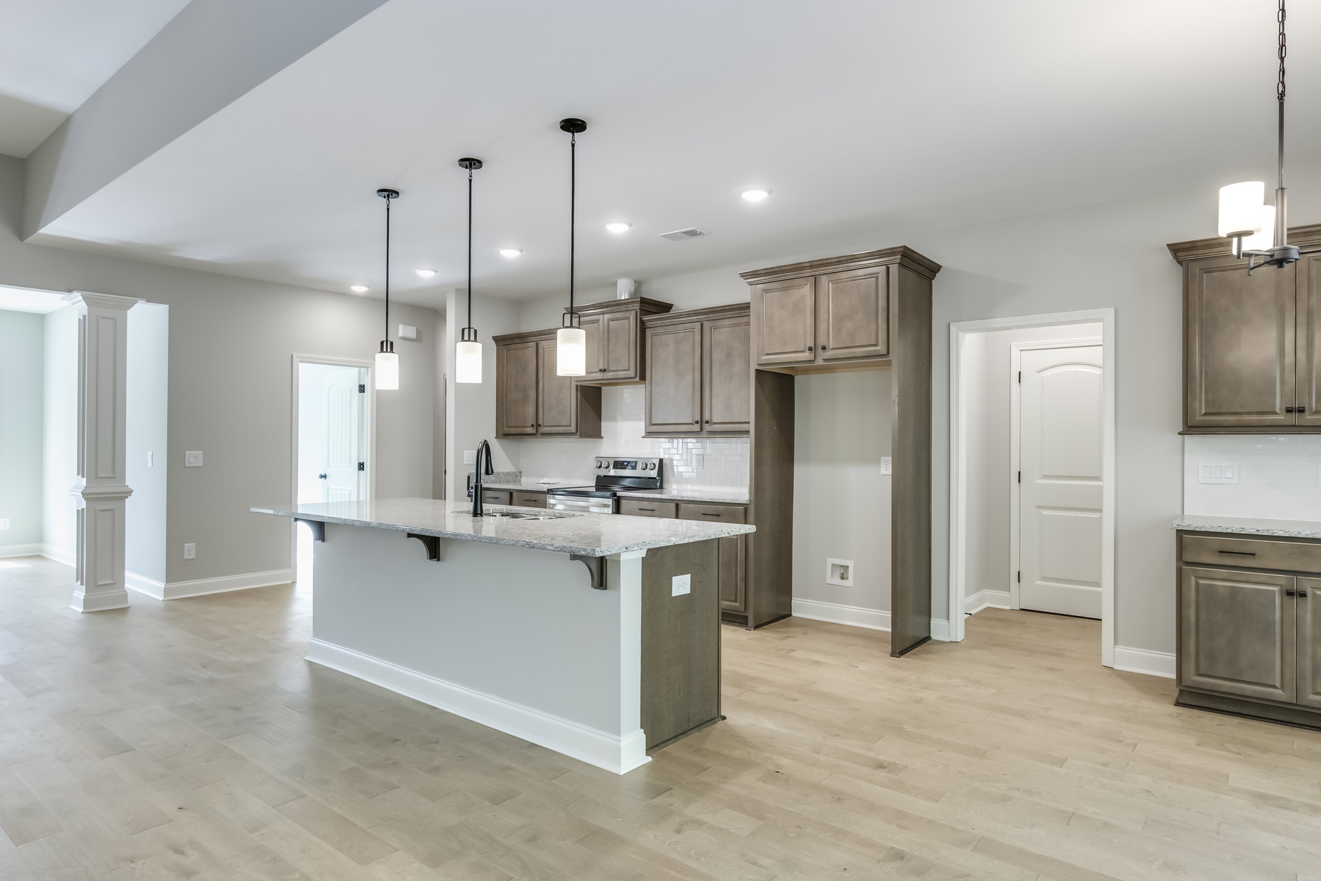 Kitchen with wood flooring, central island featuring black and white countertop, white cabinetry, white doors with black handles, ceiling-mounted light fixture, and stainless steel
