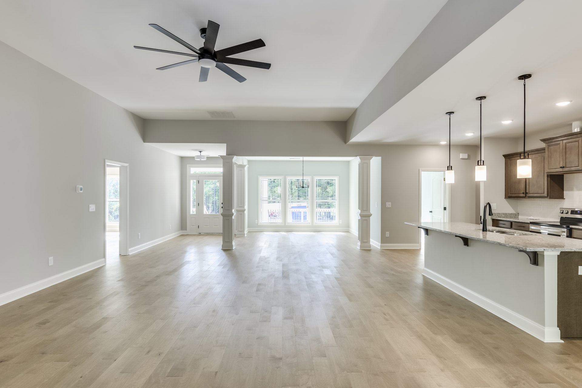 Spacious kitchen with white walls, wood flooring, ceiling fan with light, large countertop, and modern cabinetry