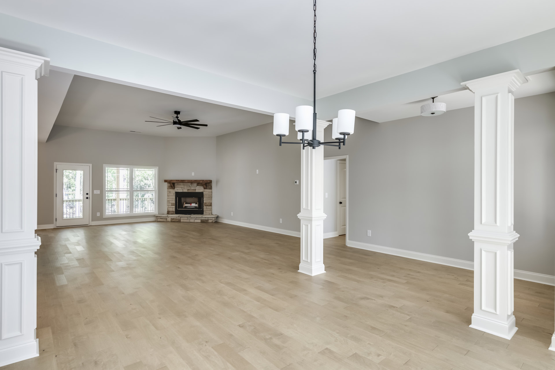 Spacious living room featuring wood laminate flooring, white plaster walls with molding, central fireplace, ceiling fan, and large windows overlooking trees